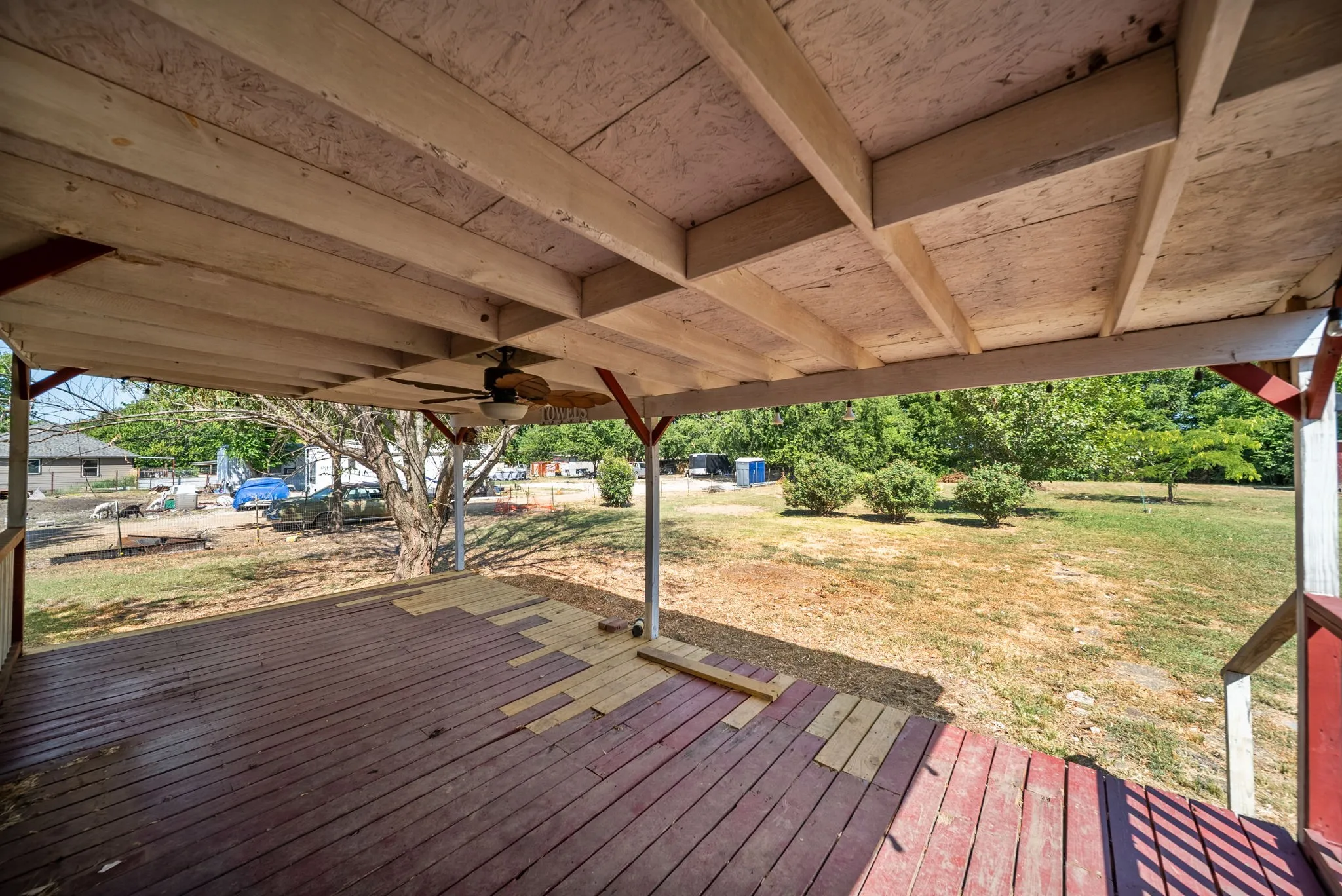 Covered porch with exposed wood beams, a ceiling fan, and a painted wood-plank deck