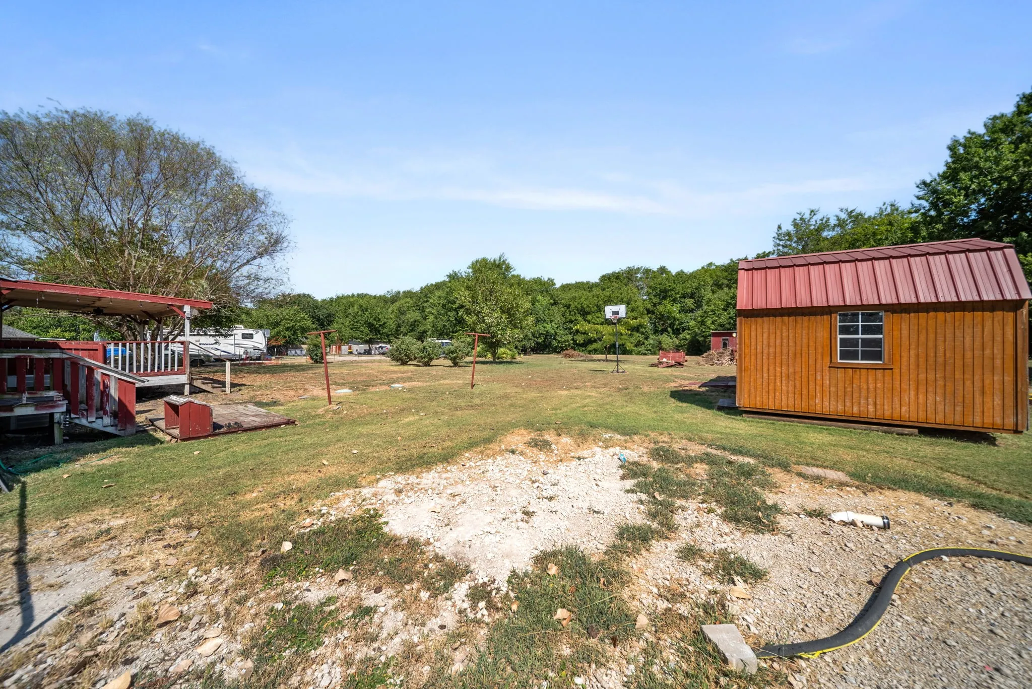 Expansive outdoor space featuring a detached storage shed with a metal roof, a covered wooden deck, and a basketball hoop