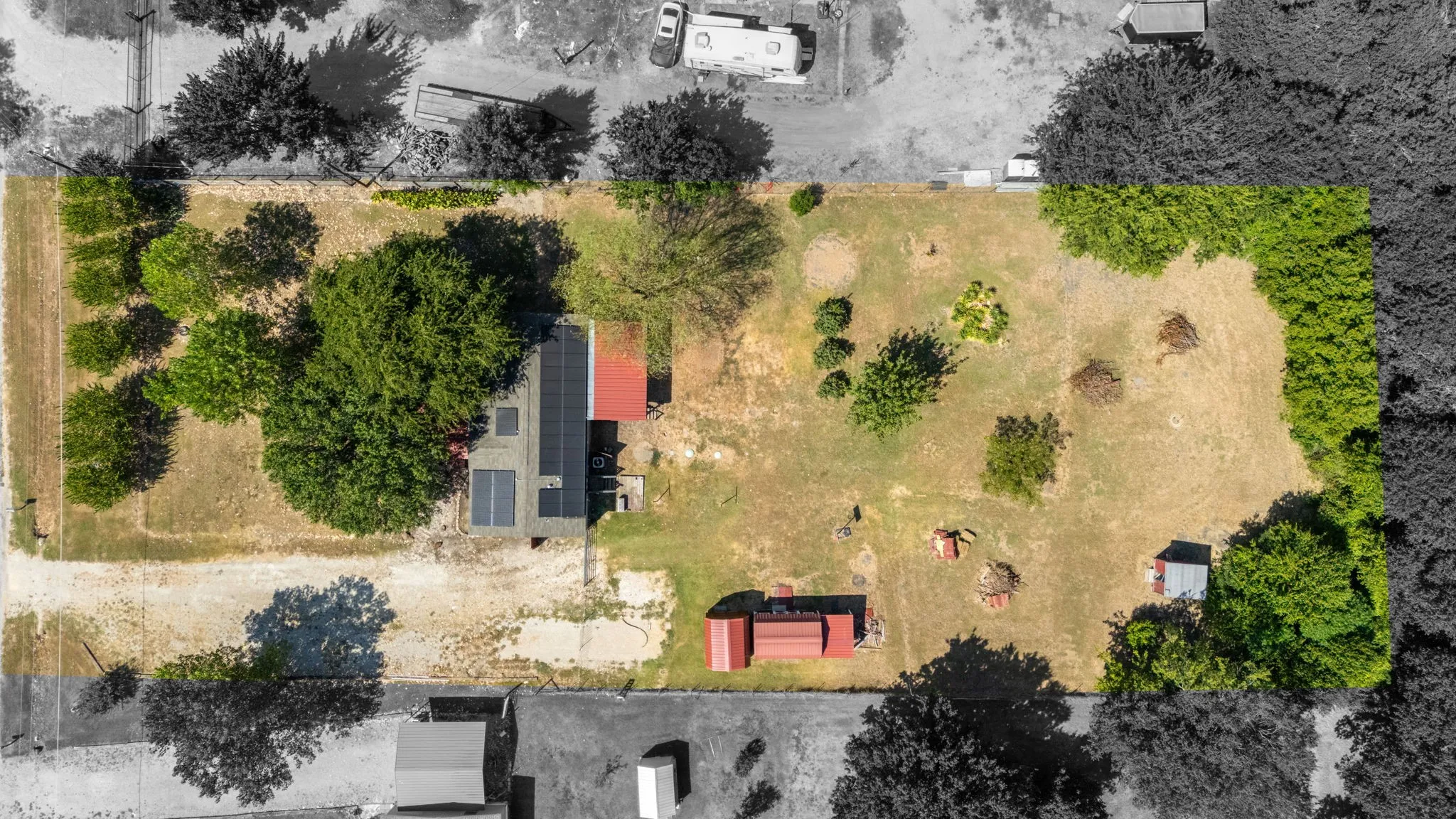 Expansive lot featuring mature trees, a red-roofed structure, solar panels, and a secondary outbuilding