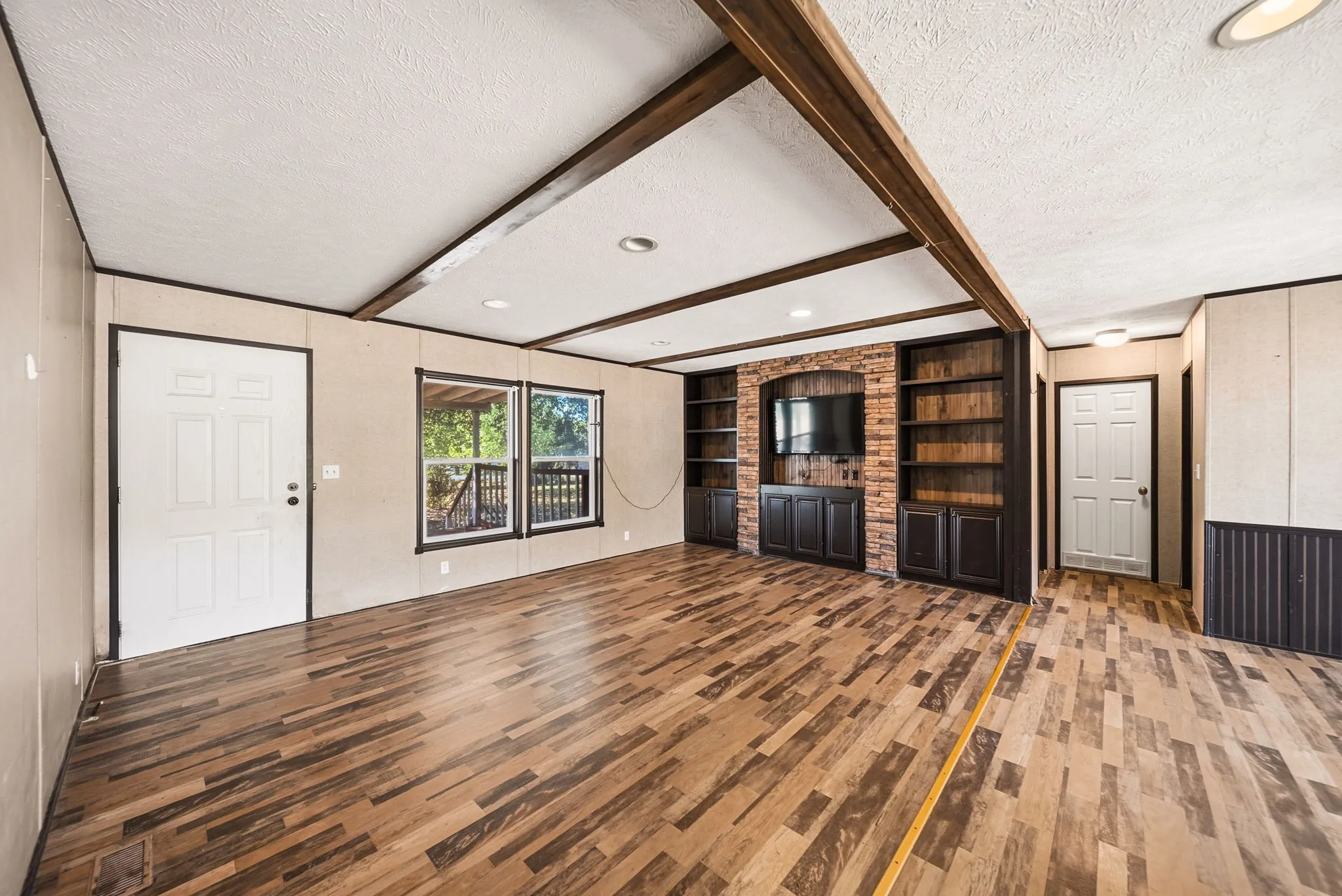 Wood-finish flooring, exposed ceiling beams, recessed lighting, built-in shelving, and a brick-finish media center