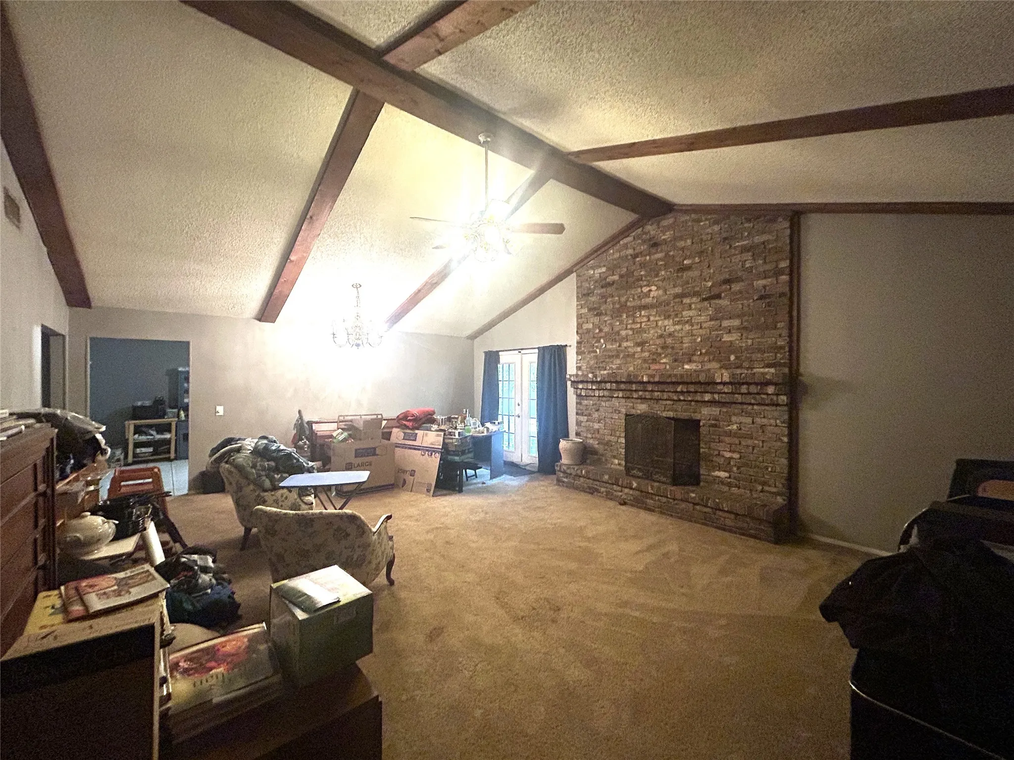 Large living room with exposed beams, wood fireplace and double doors to the porch.