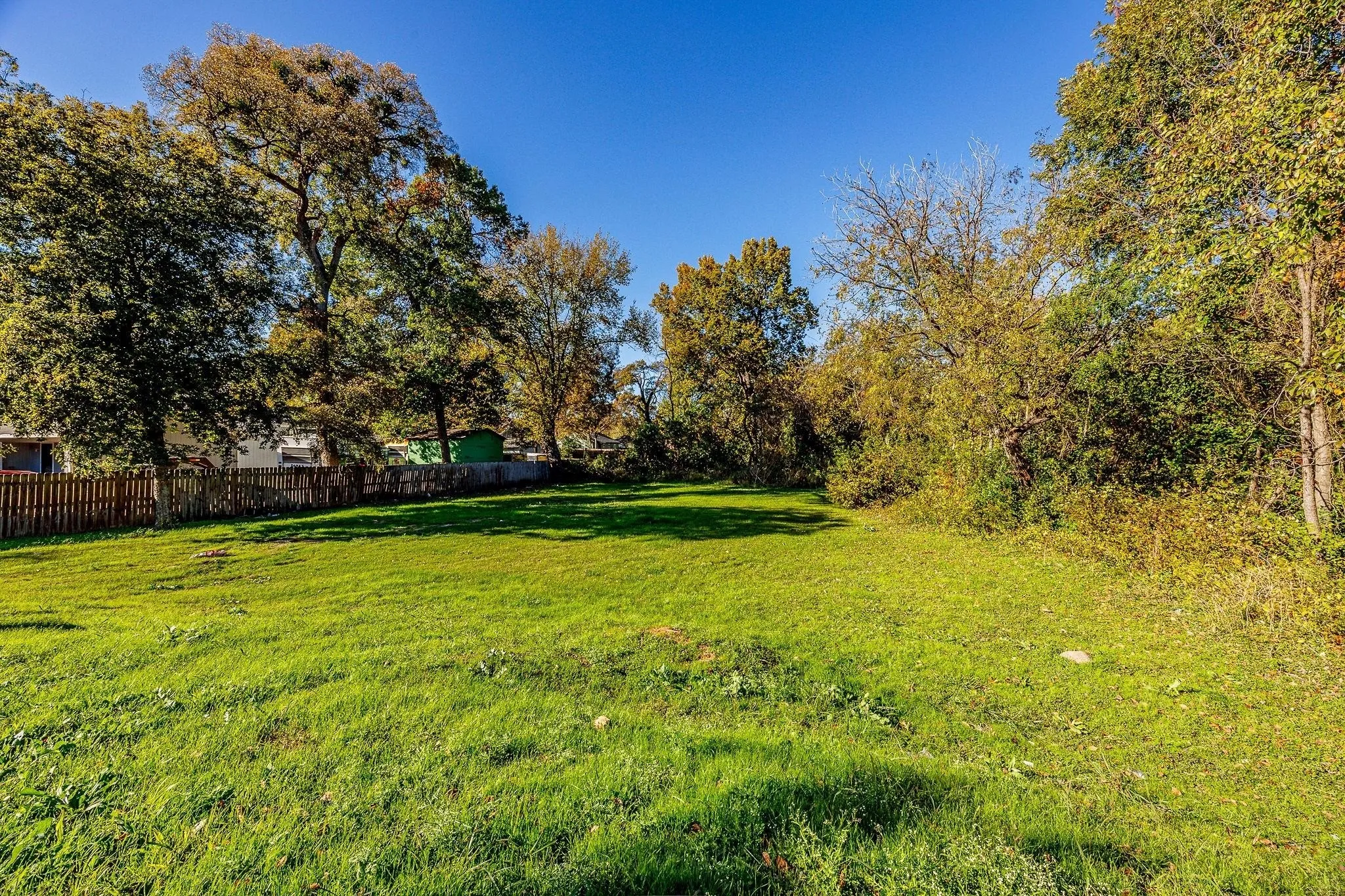 Expansive grassy lot bordered by mature trees and a wood fence