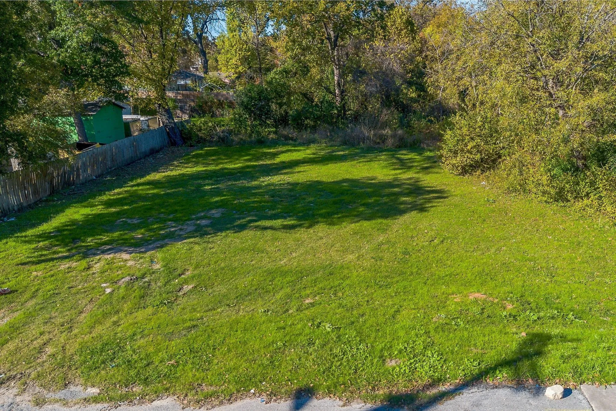 Expansive grass lot with mature trees and a partial wood fence