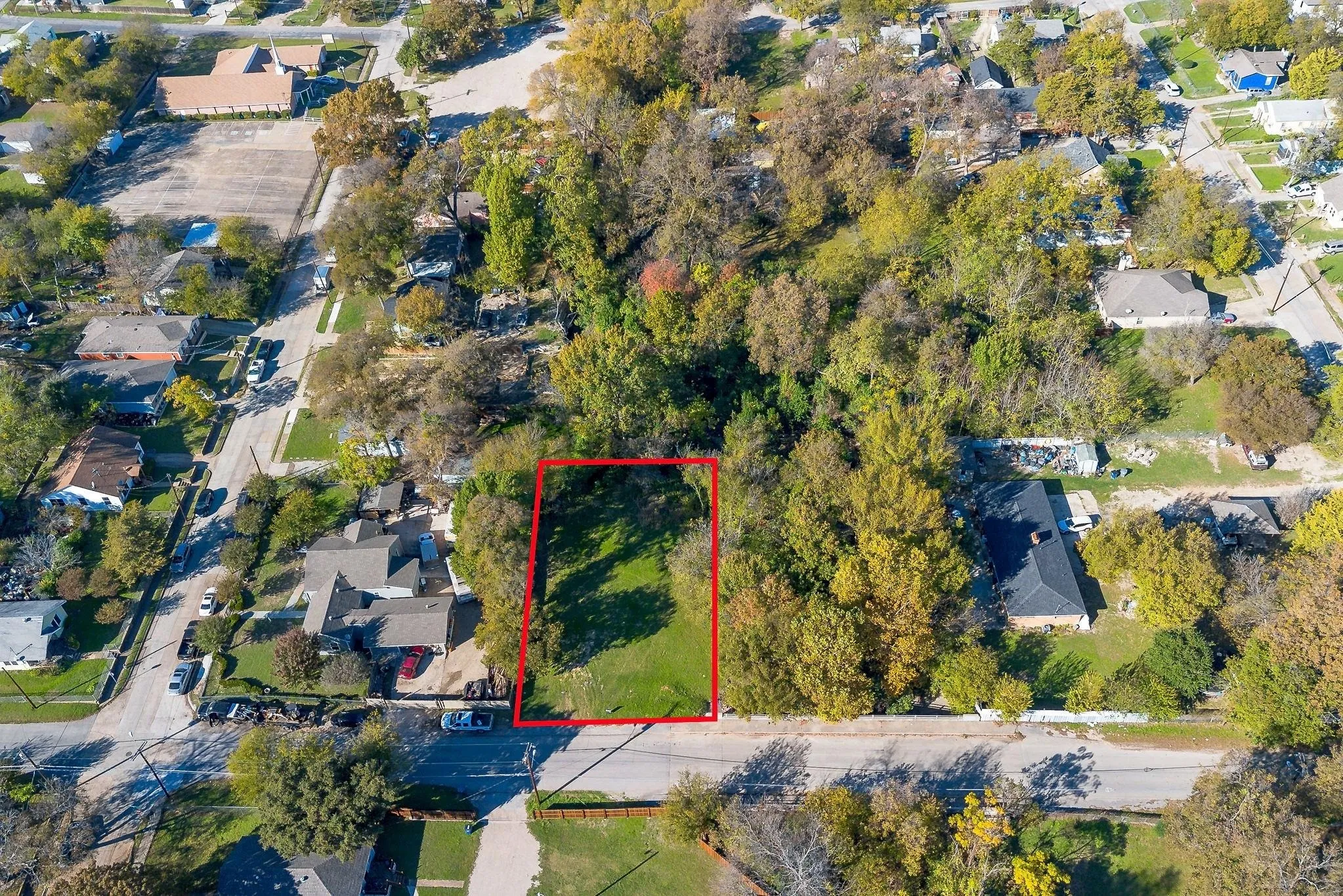 Expansive land parcel featuring a green lawn, mature trees, and street frontage