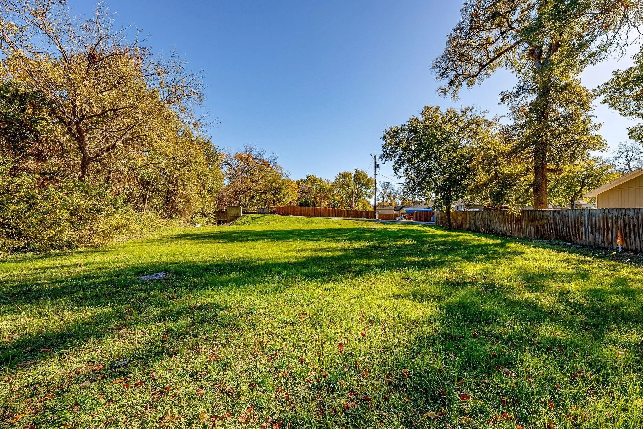 Expansive grassy lot bordered by established trees and a wood fence