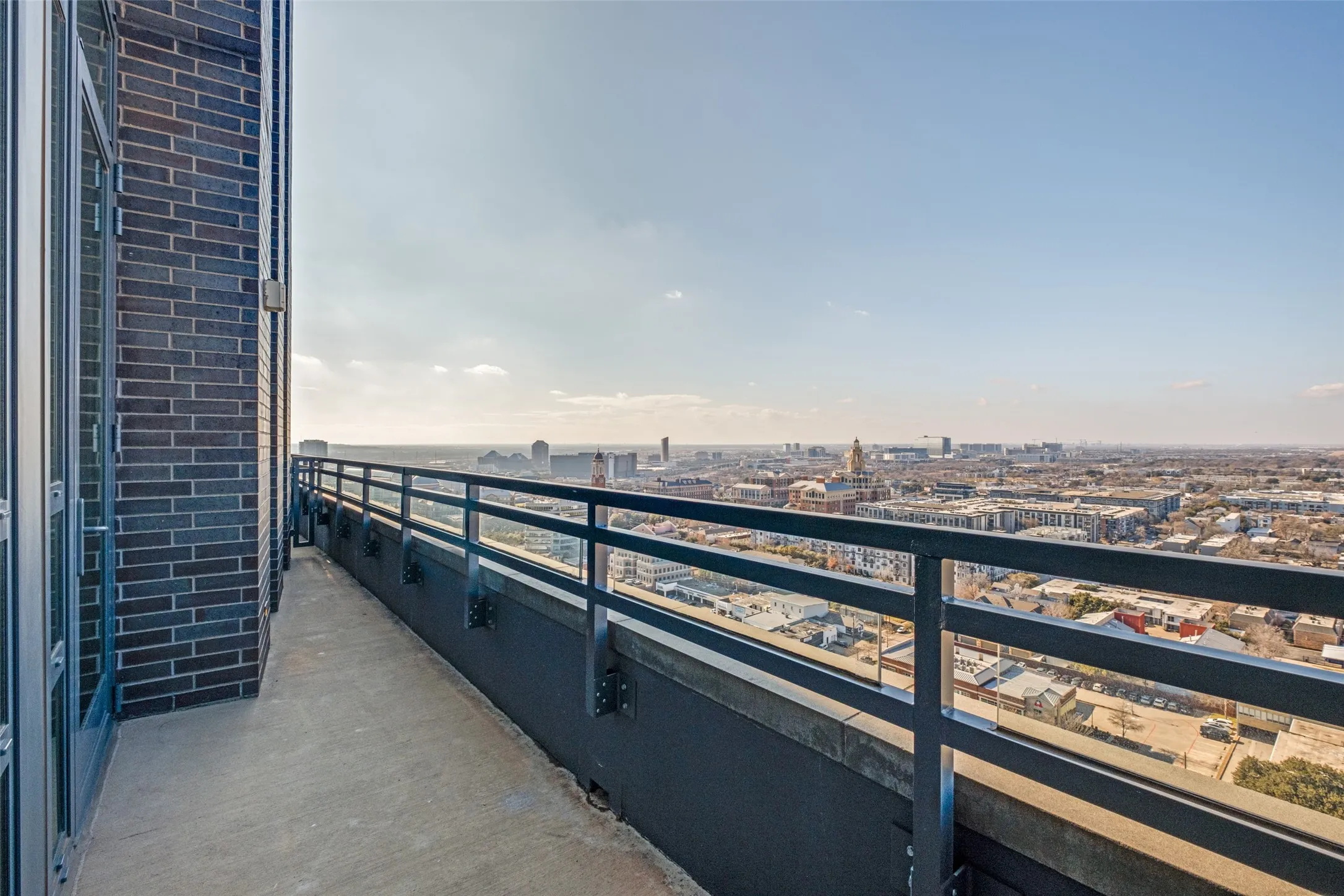 Concrete balcony with black metal railings, dark brick exterior, and expansive city surroundings
