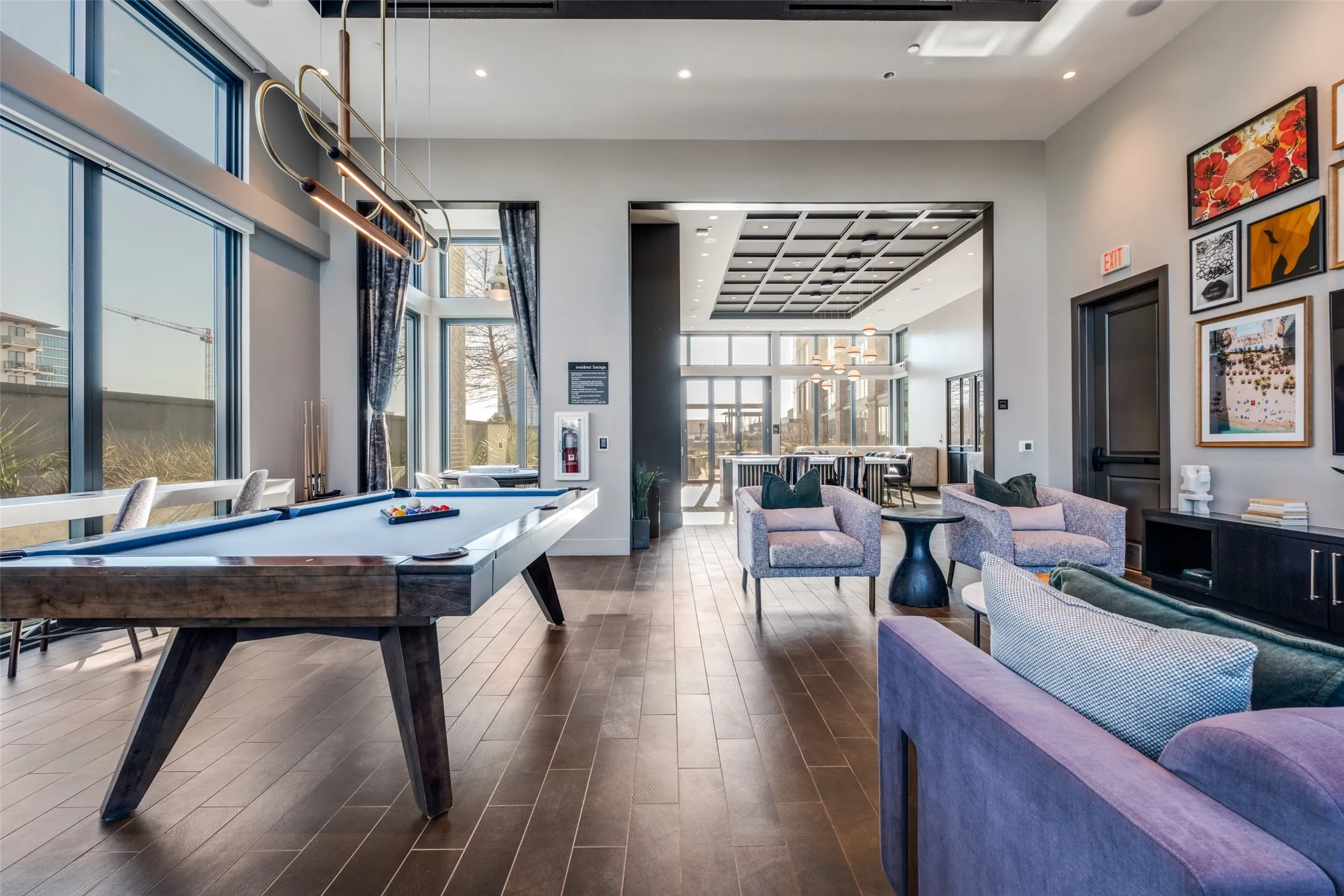 Spacious common area featuring wood-finish flooring, a billiard table, a coffered ceiling in an adjoining room, and expansive window walls