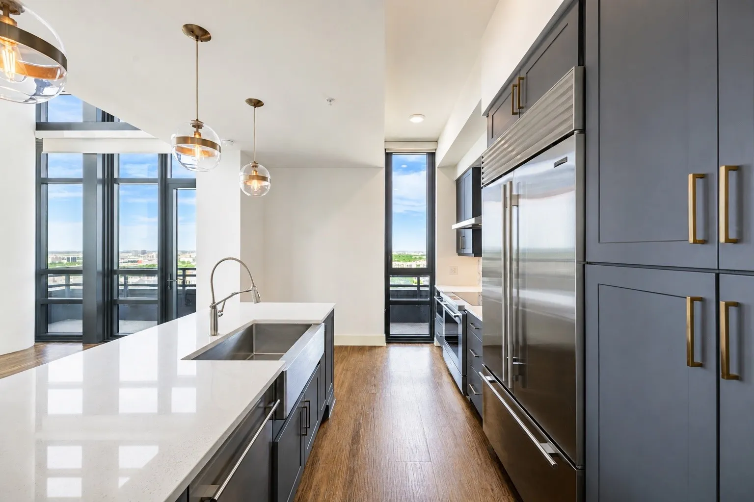 Spacious kitchen featuring an expansive island with a farmhouse sink, stainless steel appliances, dark gray cabinetry, and brass hardware