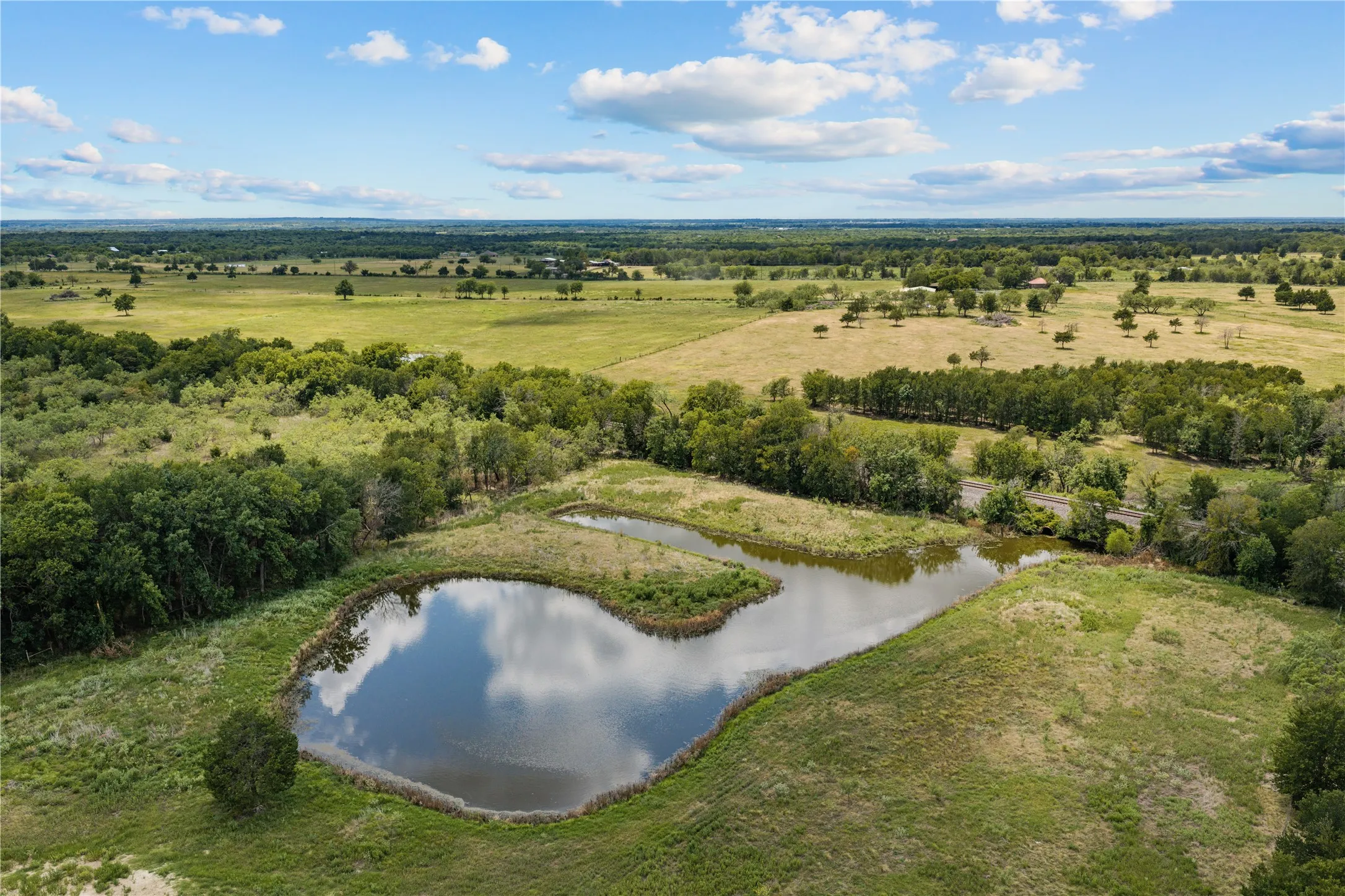 Expansive land featuring a tranquil pond, scattered mature trees, and natural vegetation