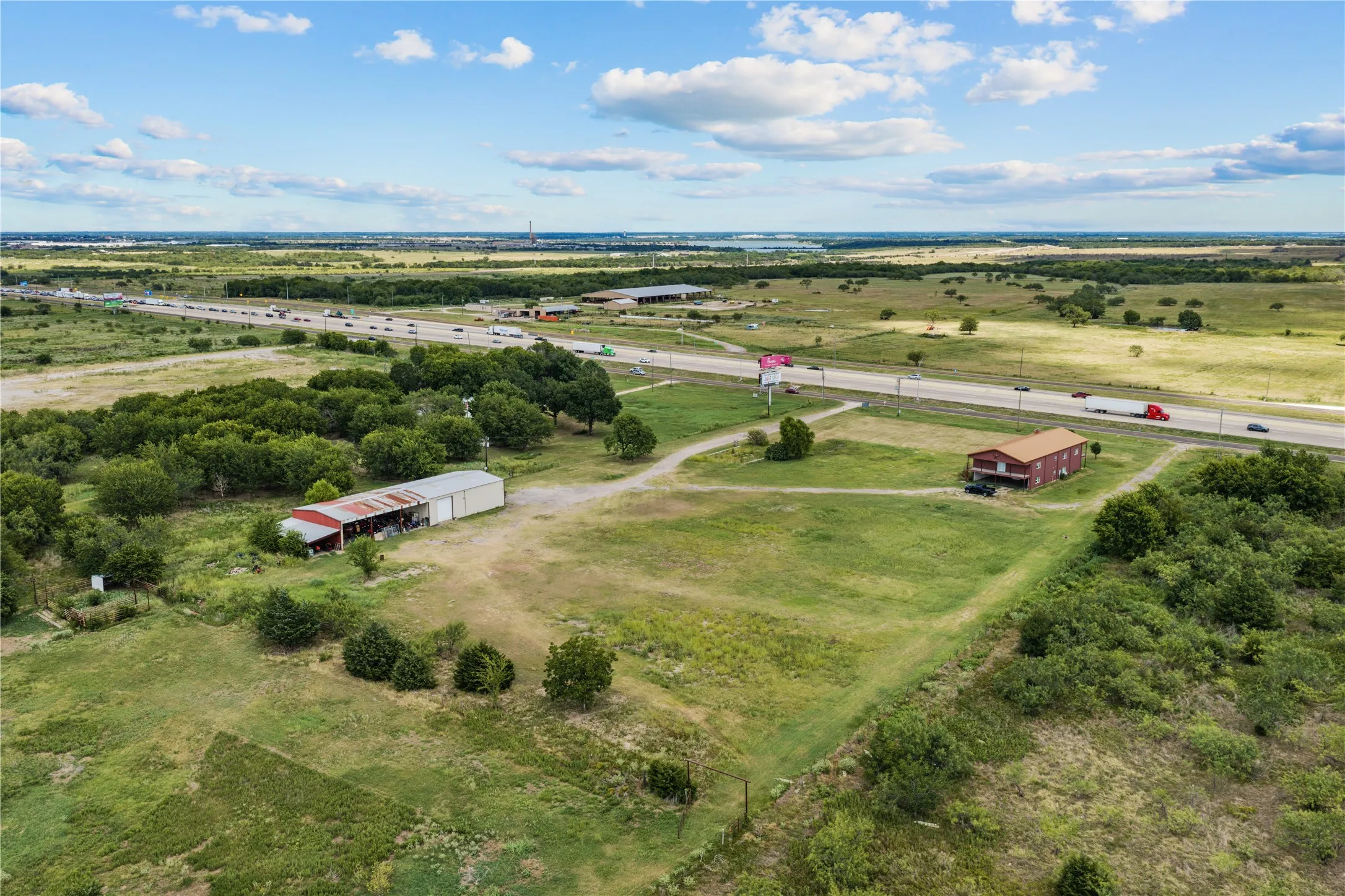 Expansive acreage featuring a two-story residence with a red exterior, a large metal barn, and mature trees