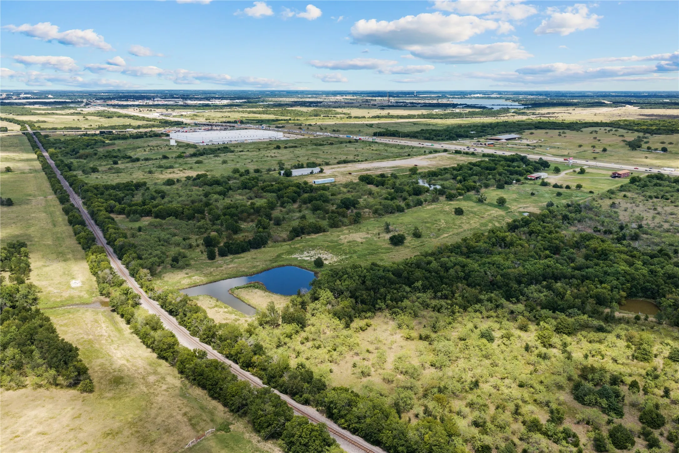 Expansive undeveloped land featuring a natural pond, mature tree lines, and a railway