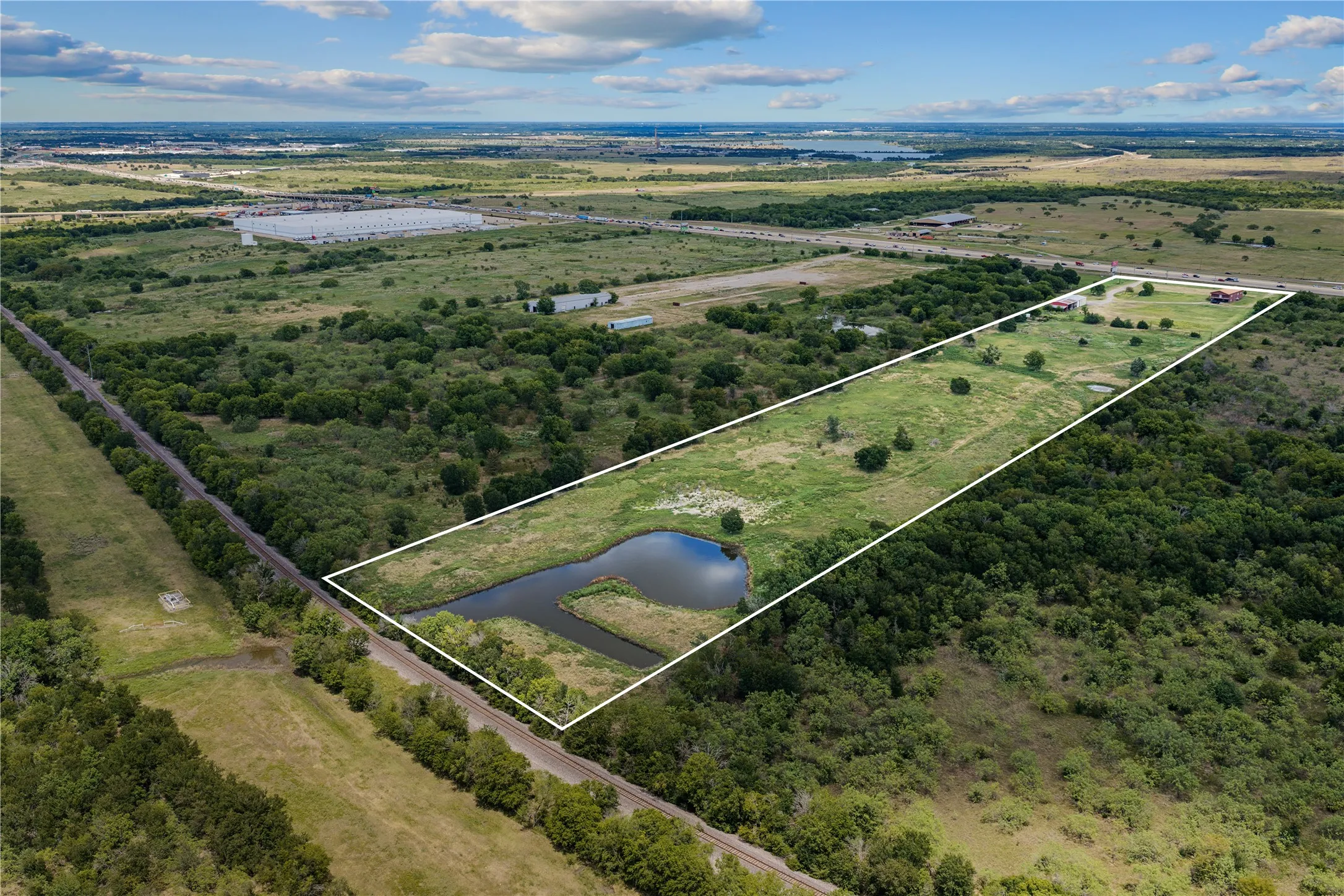 Expansive green acreage with a natural pond, bordering a wooded area, and featuring a clear boundary line