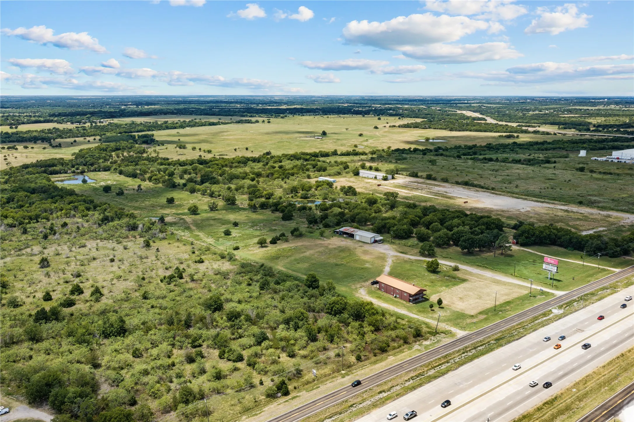 Expansive land parcel featuring existing structures, a natural pond, and mature tree coverage