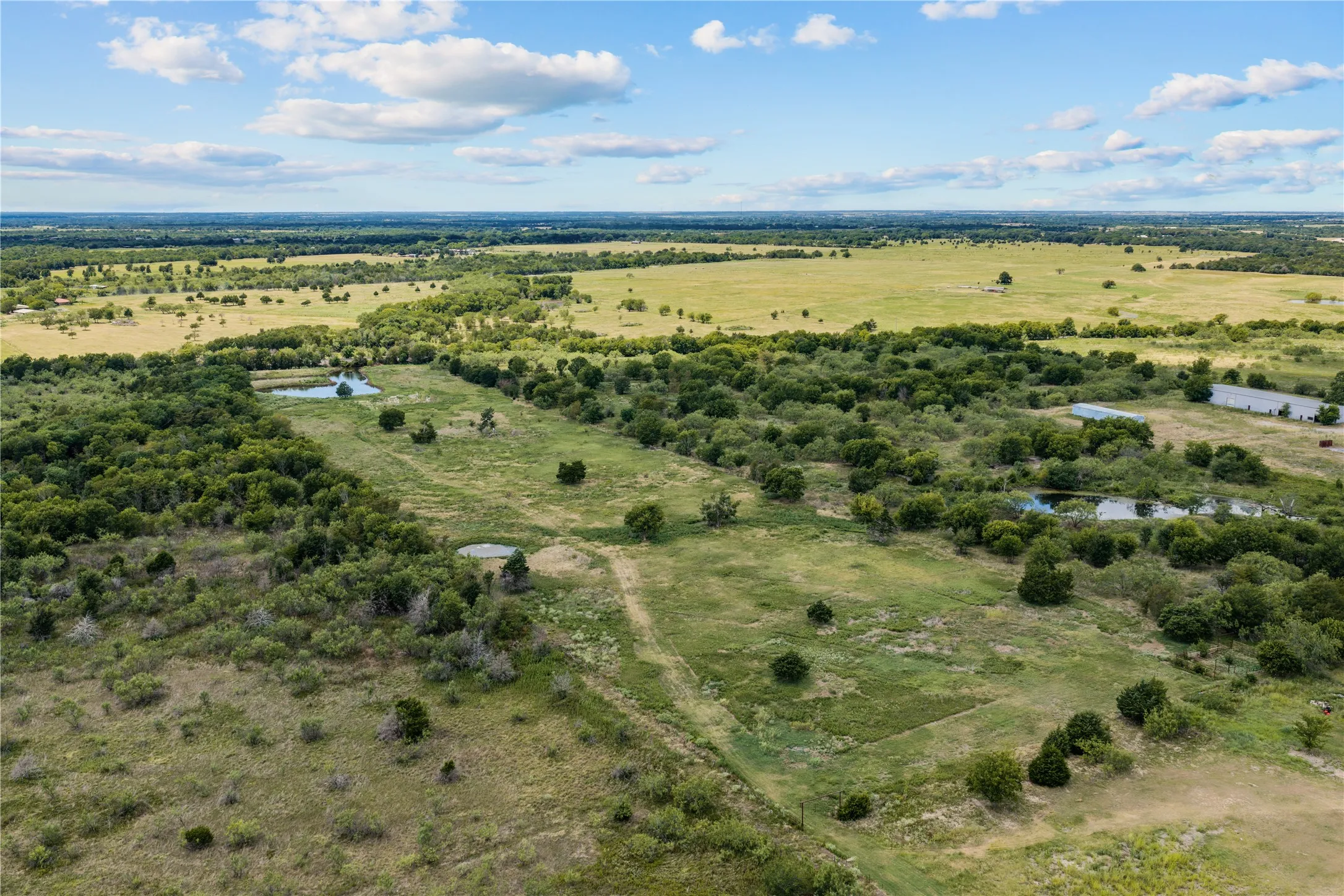 Expansive land featuring multiple ponds, scattered trees, and open grassy areas