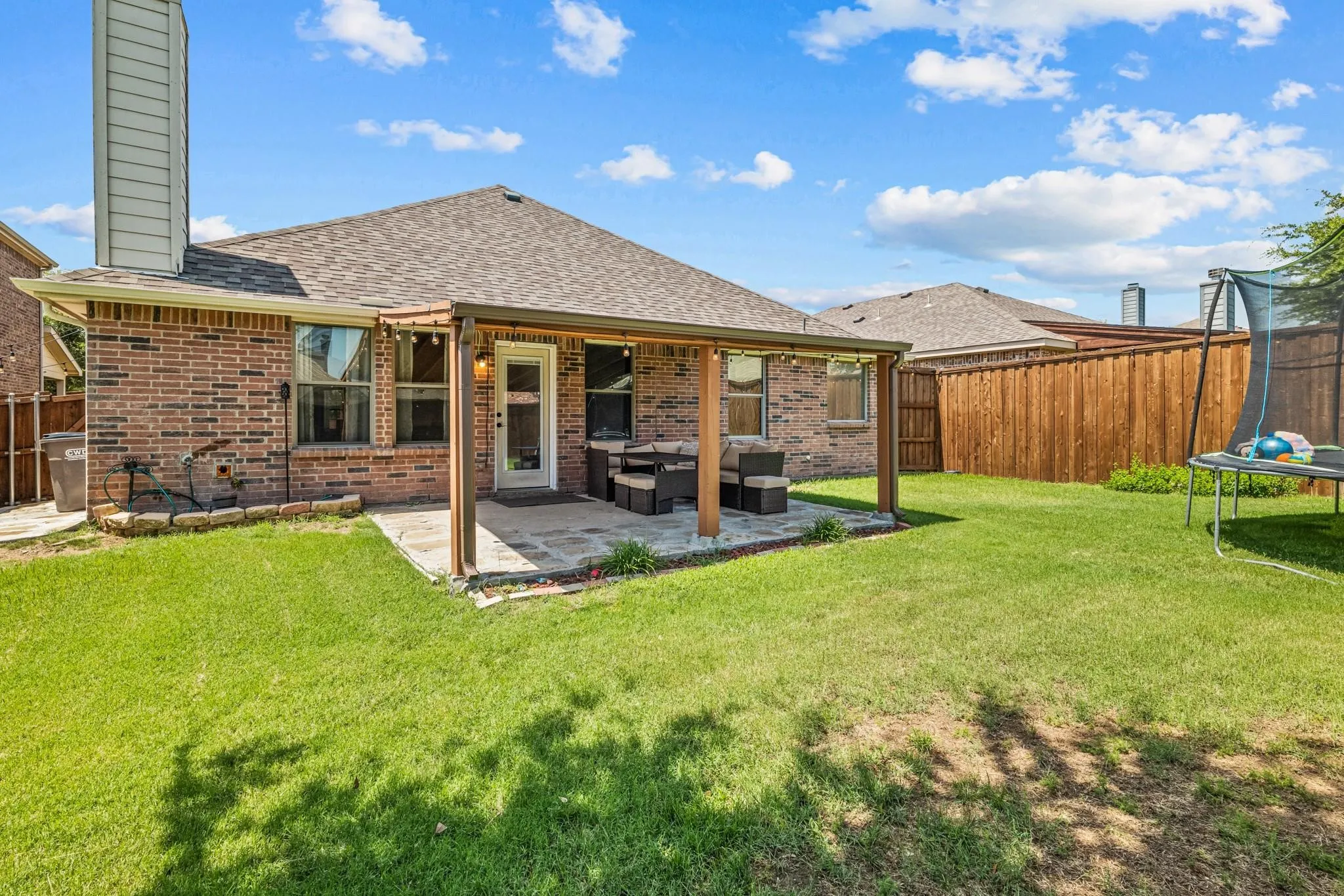 Expansive backyard featuring a covered patio, brick exterior, and wood fencing