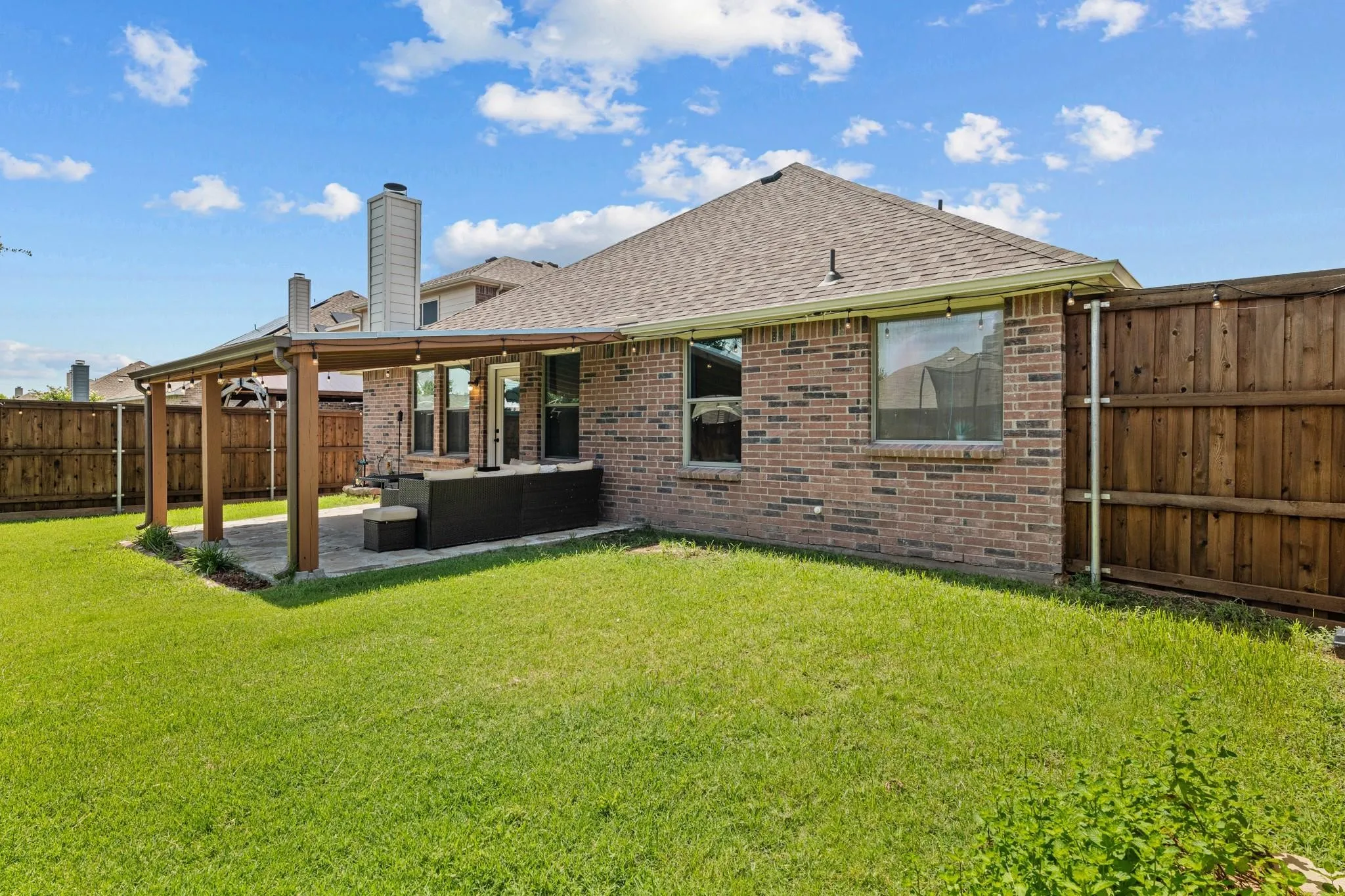 Expansive backyard featuring a covered patio, brick exterior, wood fence, and a large grassy area