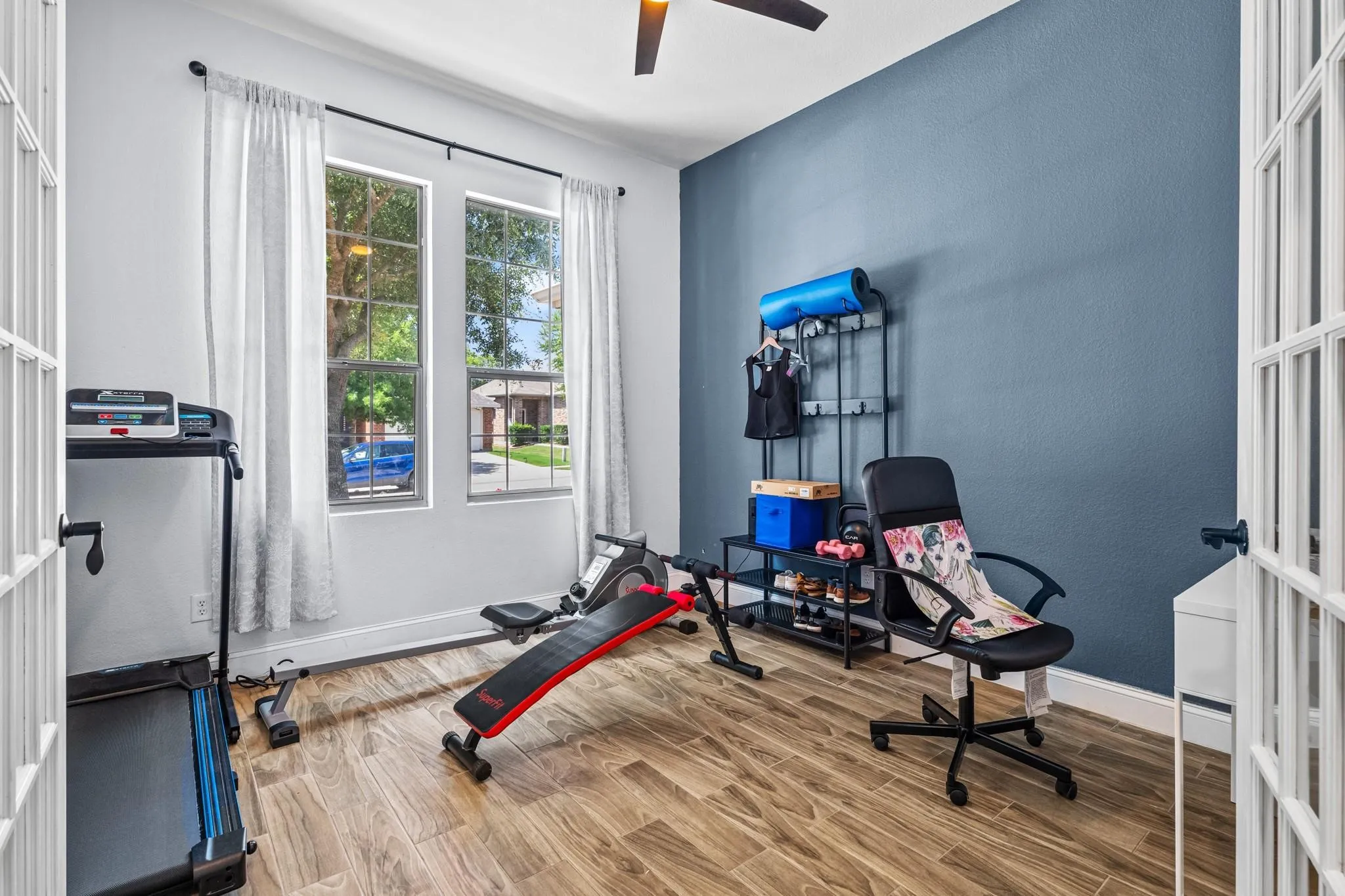 Two double-hung windows with white frames, wood-finish flooring, a ceiling fan, a blue accent wall, and white French doors