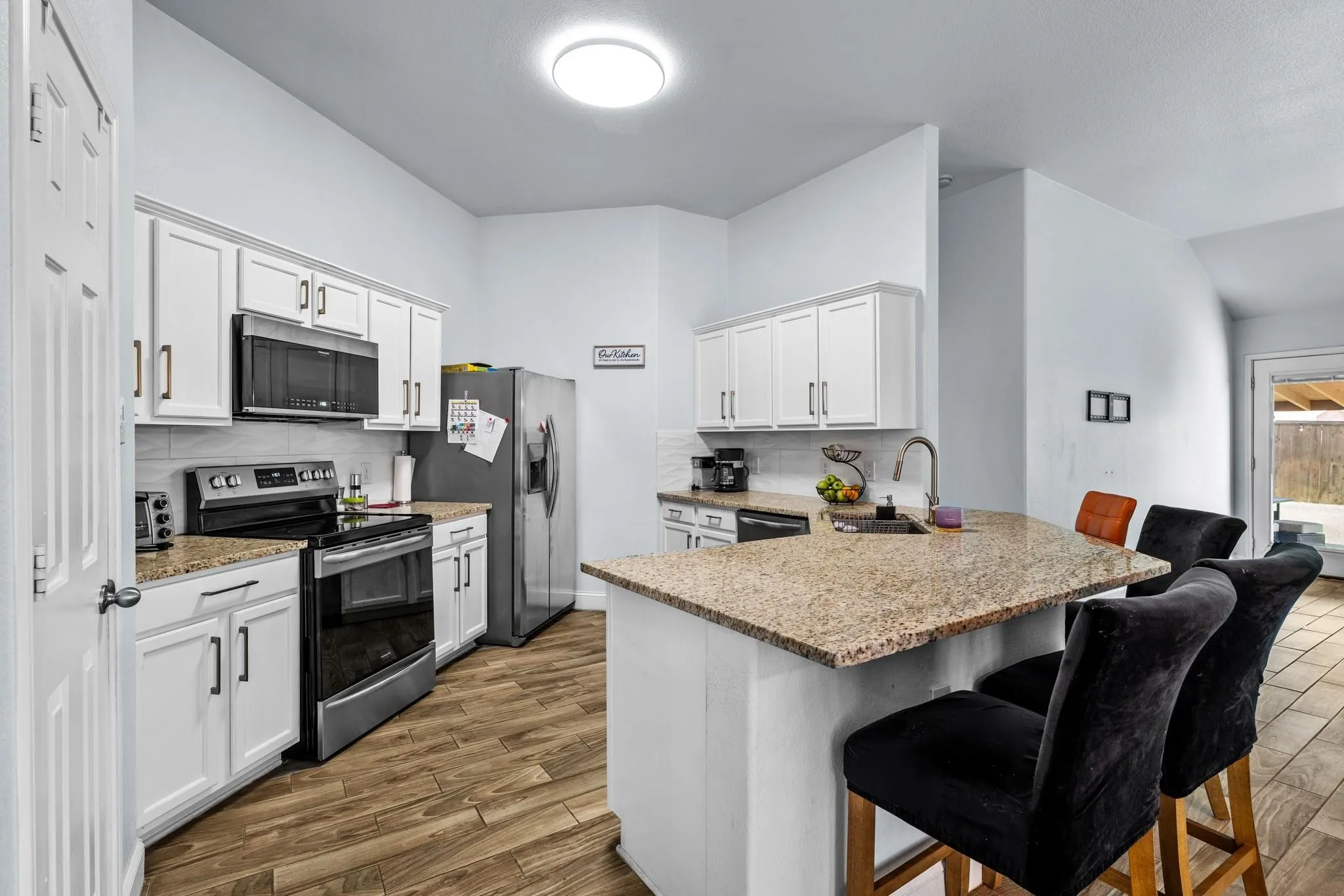 White cabinetry with dark hardware, stainless steel appliances, wood-finish flooring, light-toned countertops, and a built-in breakfast bar with a sink
