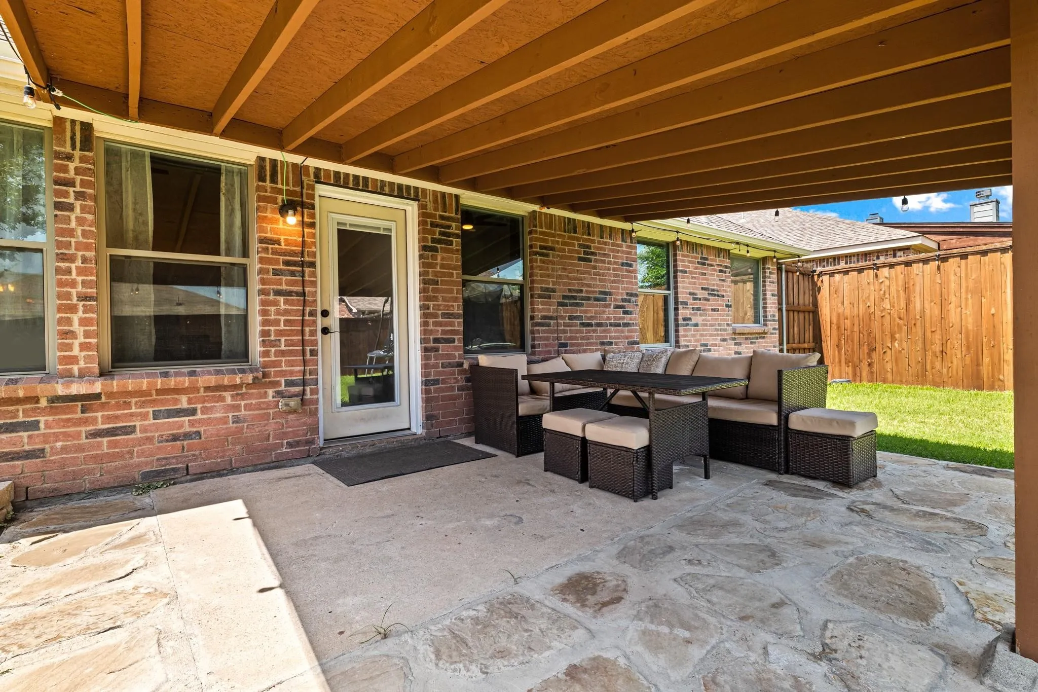 Covered patio with a flagstone and concrete surface, brick exterior, and a wood privacy fence