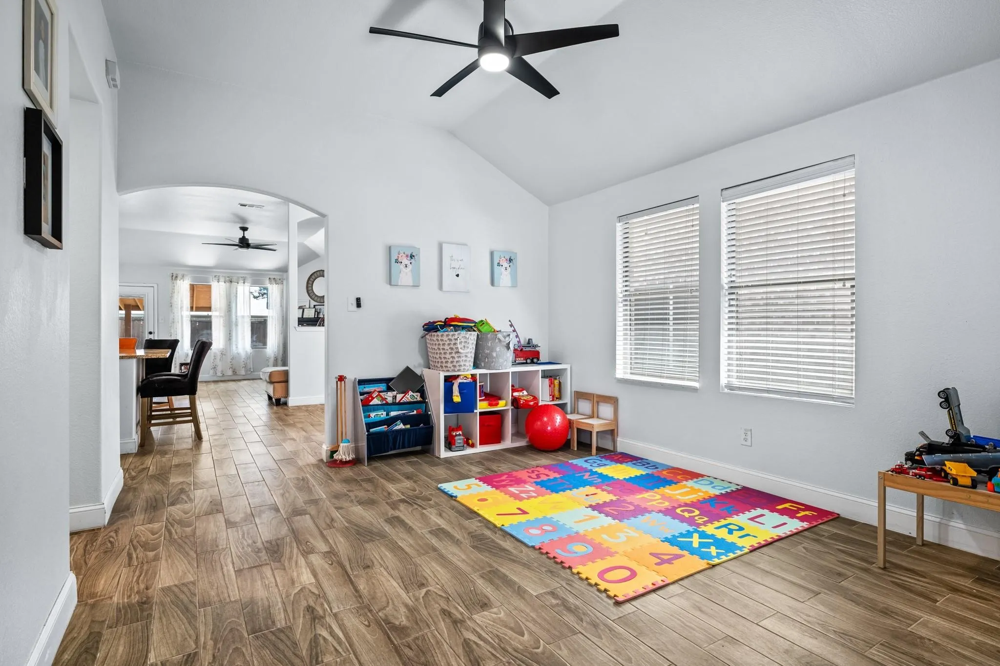 Vaulted ceiling with a black ceiling fan, two windows with blinds, wood-finish flooring, and an arched doorway