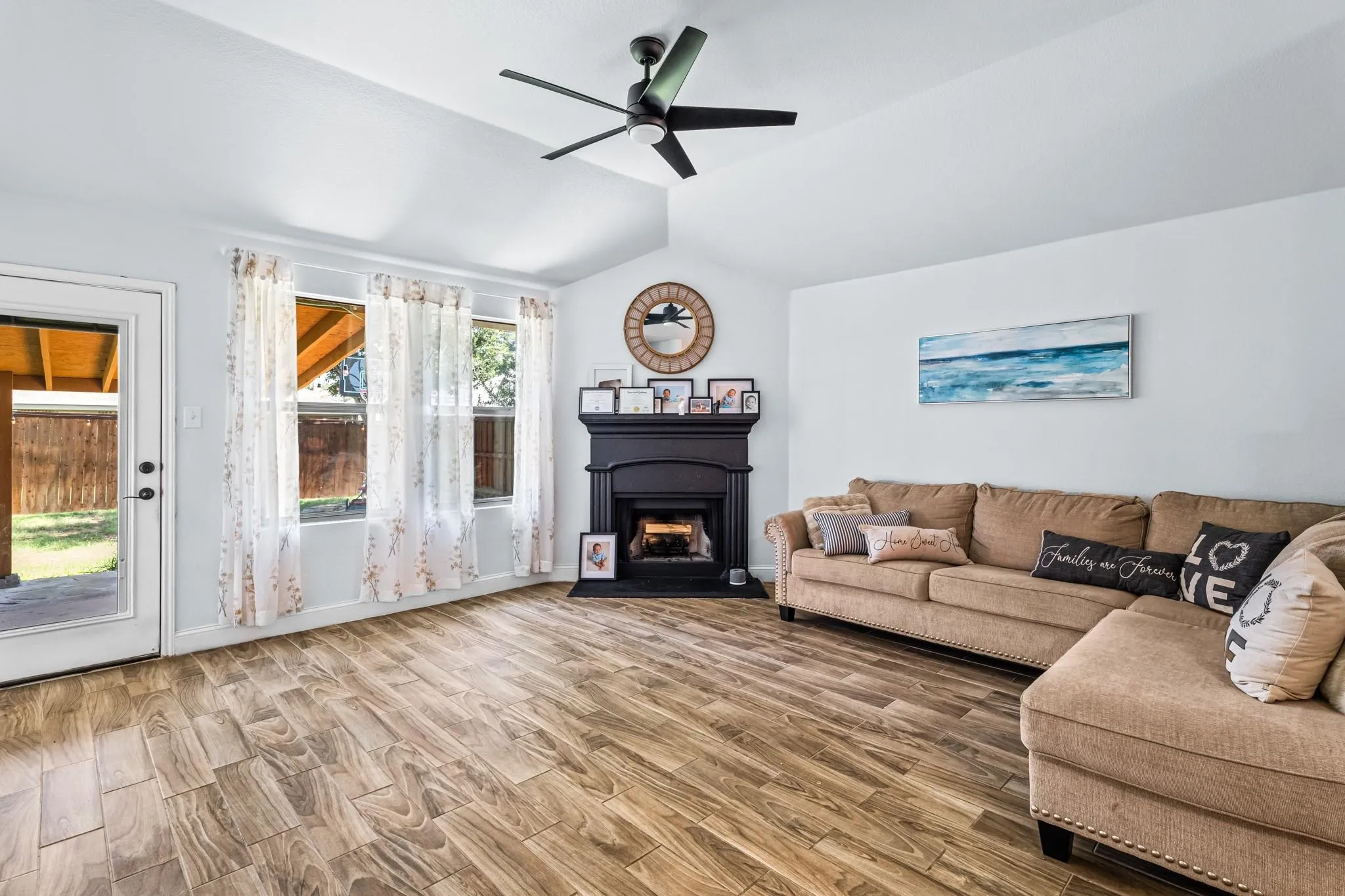 Vaulted ceiling with a ceiling fan, wood-finish flooring, multiple windows, and a black fireplace with a mantel