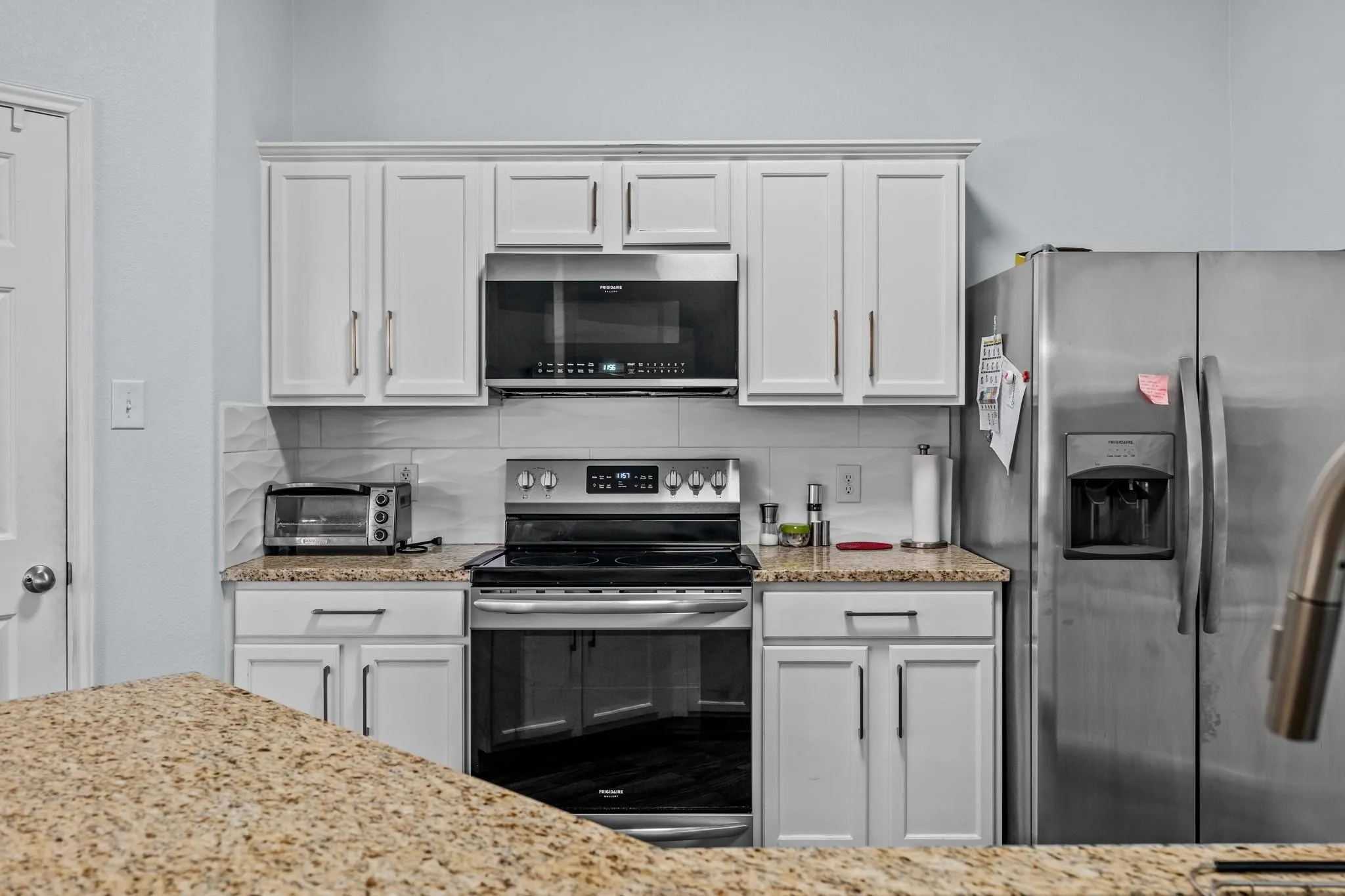 White shaker cabinetry with modern pulls, granite-finish countertops, stainless steel appliances, and a tiled backsplash
