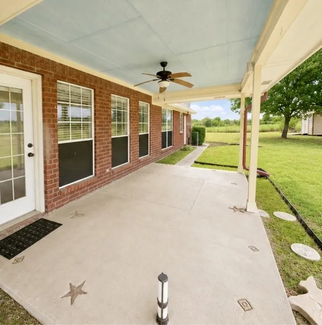 Expansive covered patio featuring a ceiling fan, brick exterior, multiple windows, and a concrete surface with decorative inlays