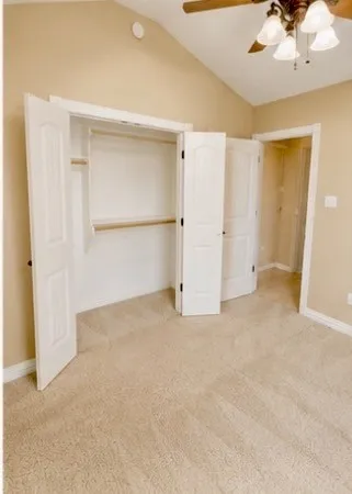 Vaulted ceiling, ceiling fan with integrated lighting, built-in closet storage, light-toned carpeting, and paneled interior doors