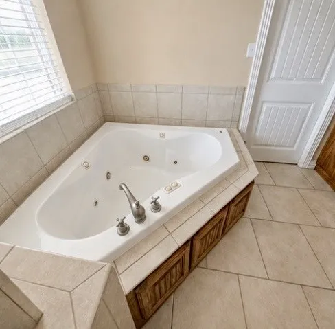 Built-in corner soaking tub with integrated jets, tile surround, and wood-finish cabinetry