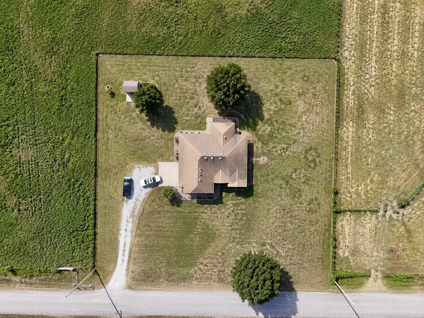 Single-story property with a light-colored roof, surrounded by expansive green space, featuring a gravel driveway and an additional detached structure