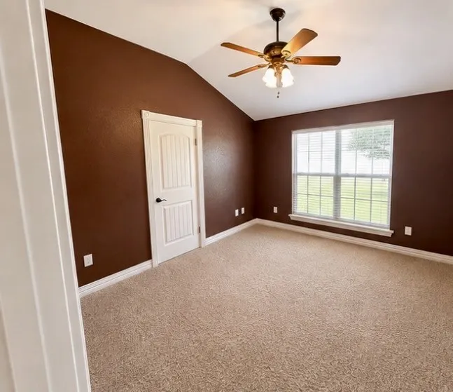 Vaulted ceiling with an integrated ceiling fan and light fixture, window with blinds, paneled interior door, and neutral-toned carpeting