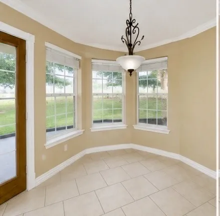 Bay window with multiple windows, crown molding, a decorative ceiling light fixture, tile flooring, and a wood-framed glass door