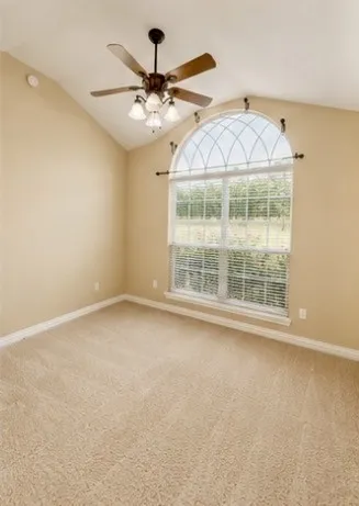 Vaulted ceiling, arched window with decorative grille, ceiling fan with integrated lighting, carpeted flooring, and white baseboards