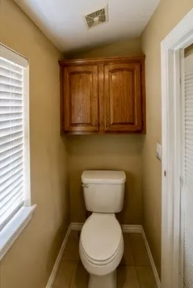 Warm-toned walls with a white toilet, wood-finish cabinetry, and tiled flooring