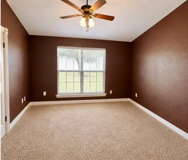Expansive room featuring wall-to-wall carpeting, a large window with blinds, and a ceiling fan with integrated lighting