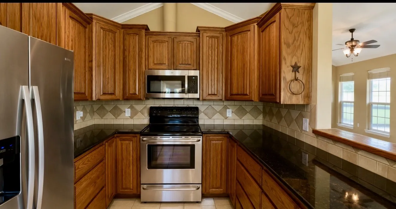 Kitchen featuring wood cabinetry, stainless steel appliances, dark granite countertops, and a tiled backsplash