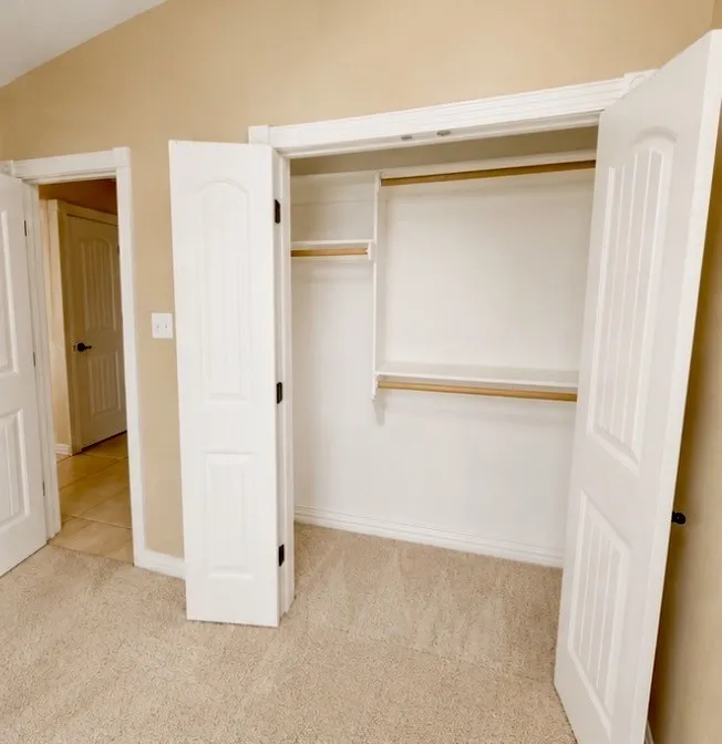 Built-in closet system with shelving and two hanging rods, carpet flooring, and paneled interior doors