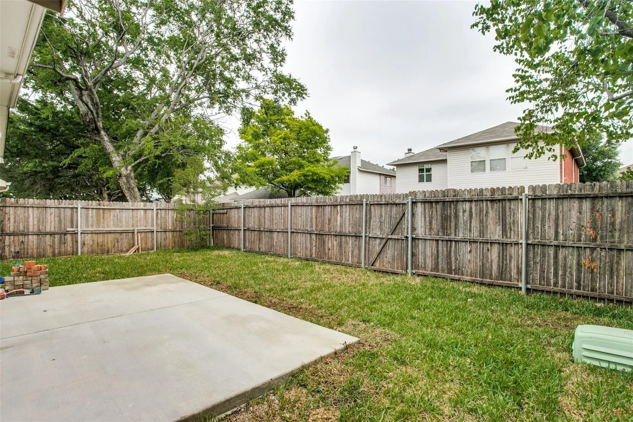 Expansive backyard featuring a wood fence, mature trees, and a concrete patio