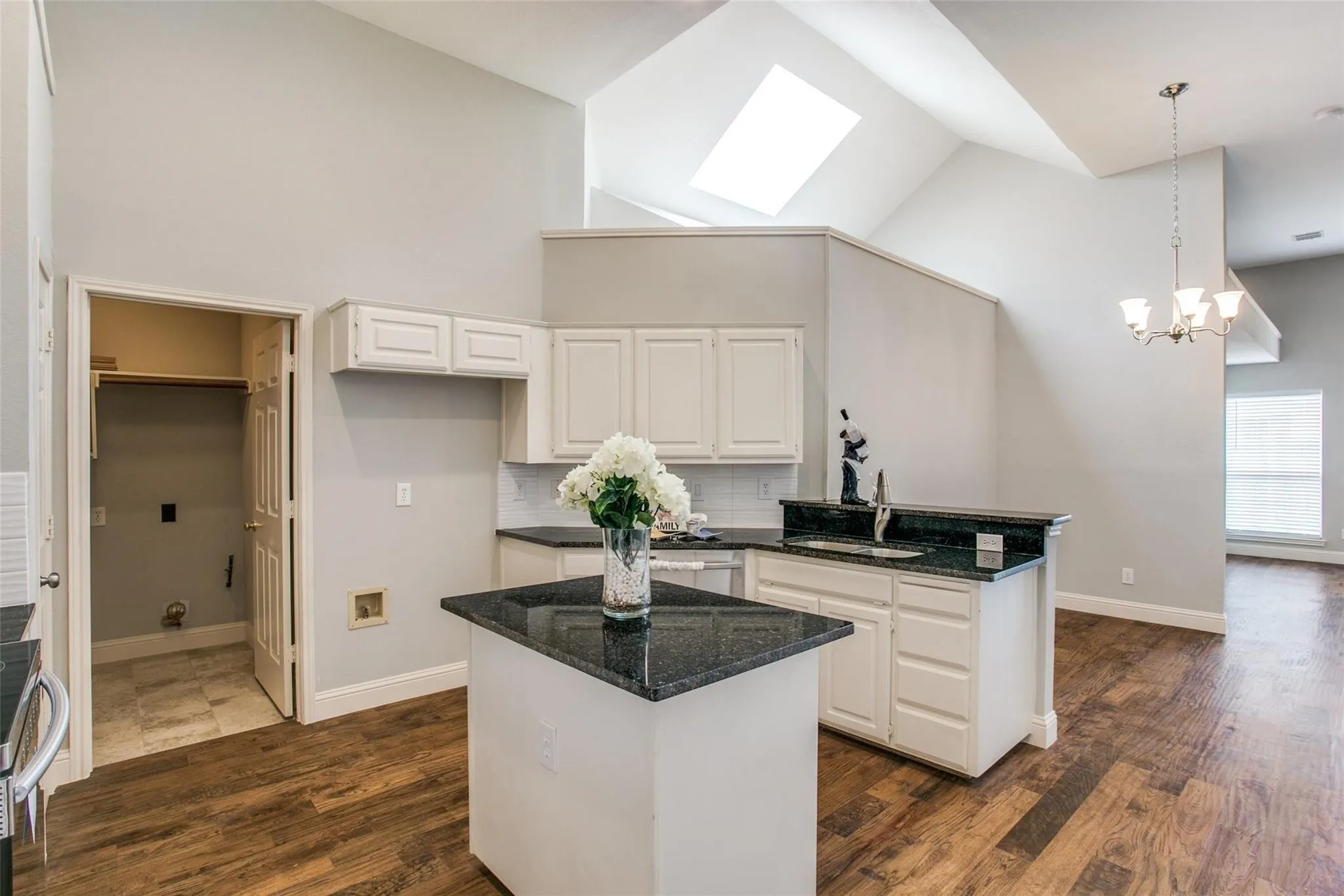 Vaulted ceilings with a skylight, wood-finish flooring, white cabinetry, dark granite countertops, and a tile backsplash