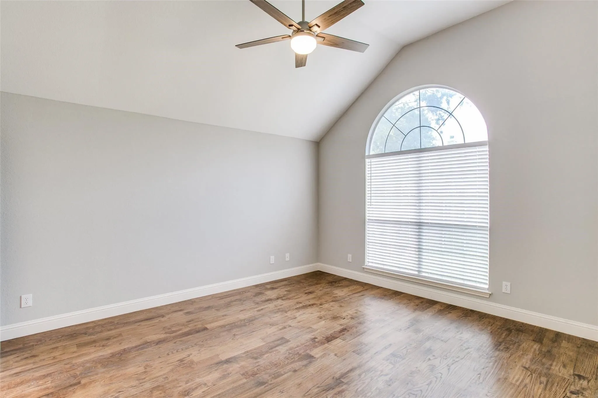 Vaulted ceiling with an attached ceiling fan, large arched window with blinds, and wood-finish flooring