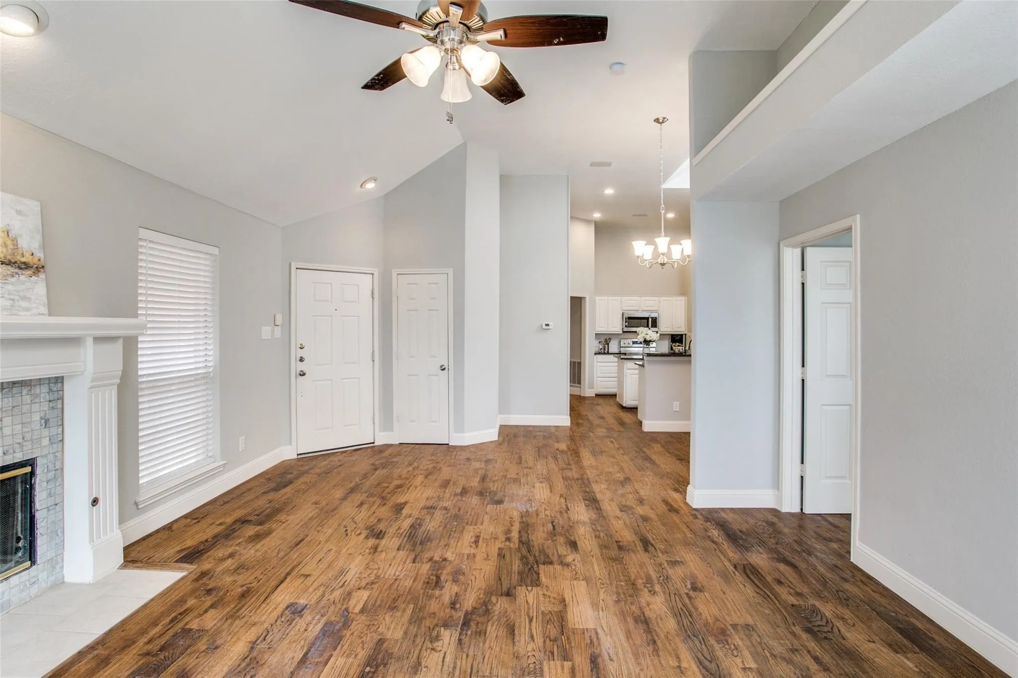 Wood-finish flooring, vaulted ceiling, fireplace with tile surround, ceiling fan, and recessed lighting