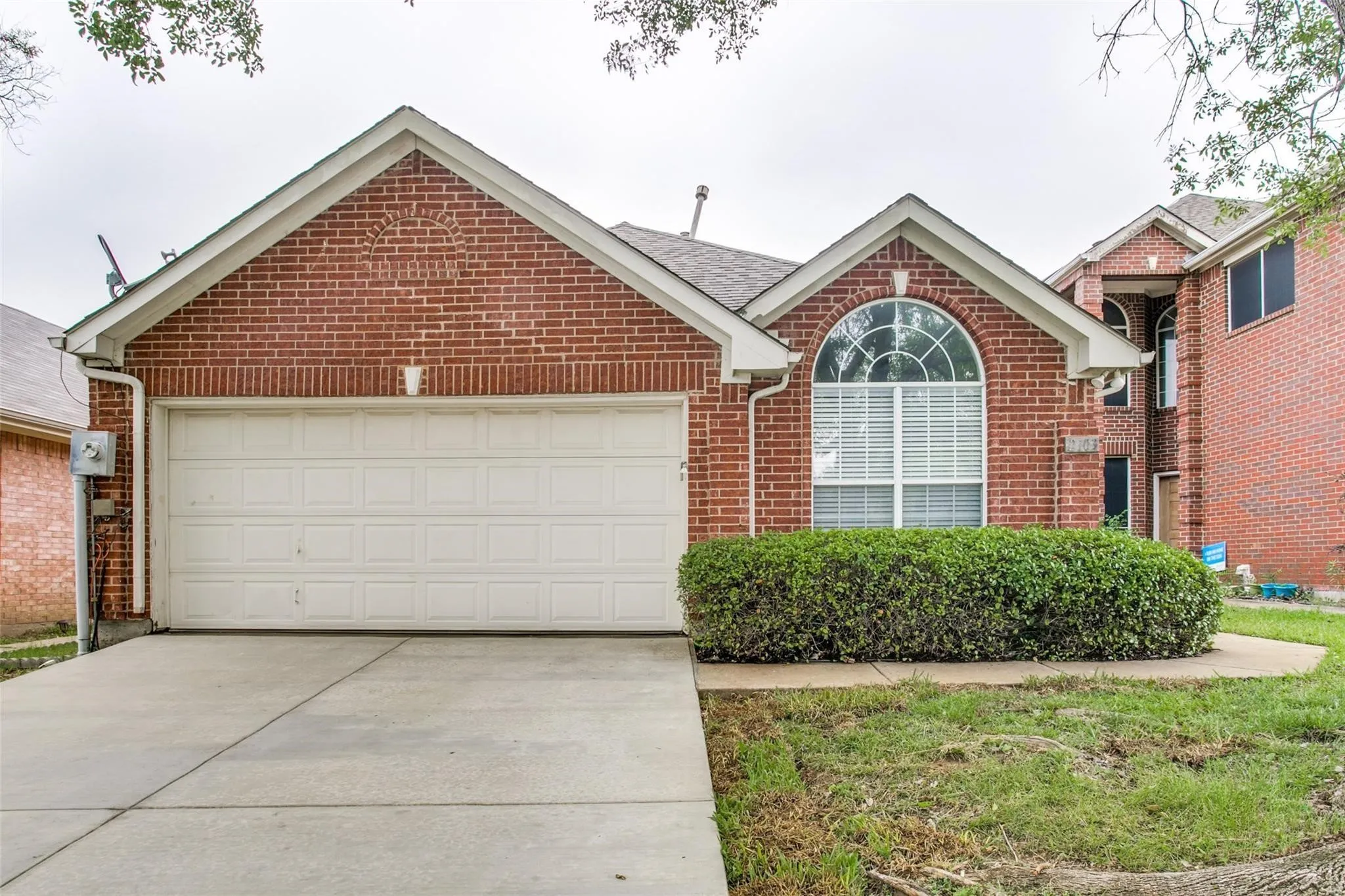Brick exterior with an arched window, white window blinds, and a two-car garage