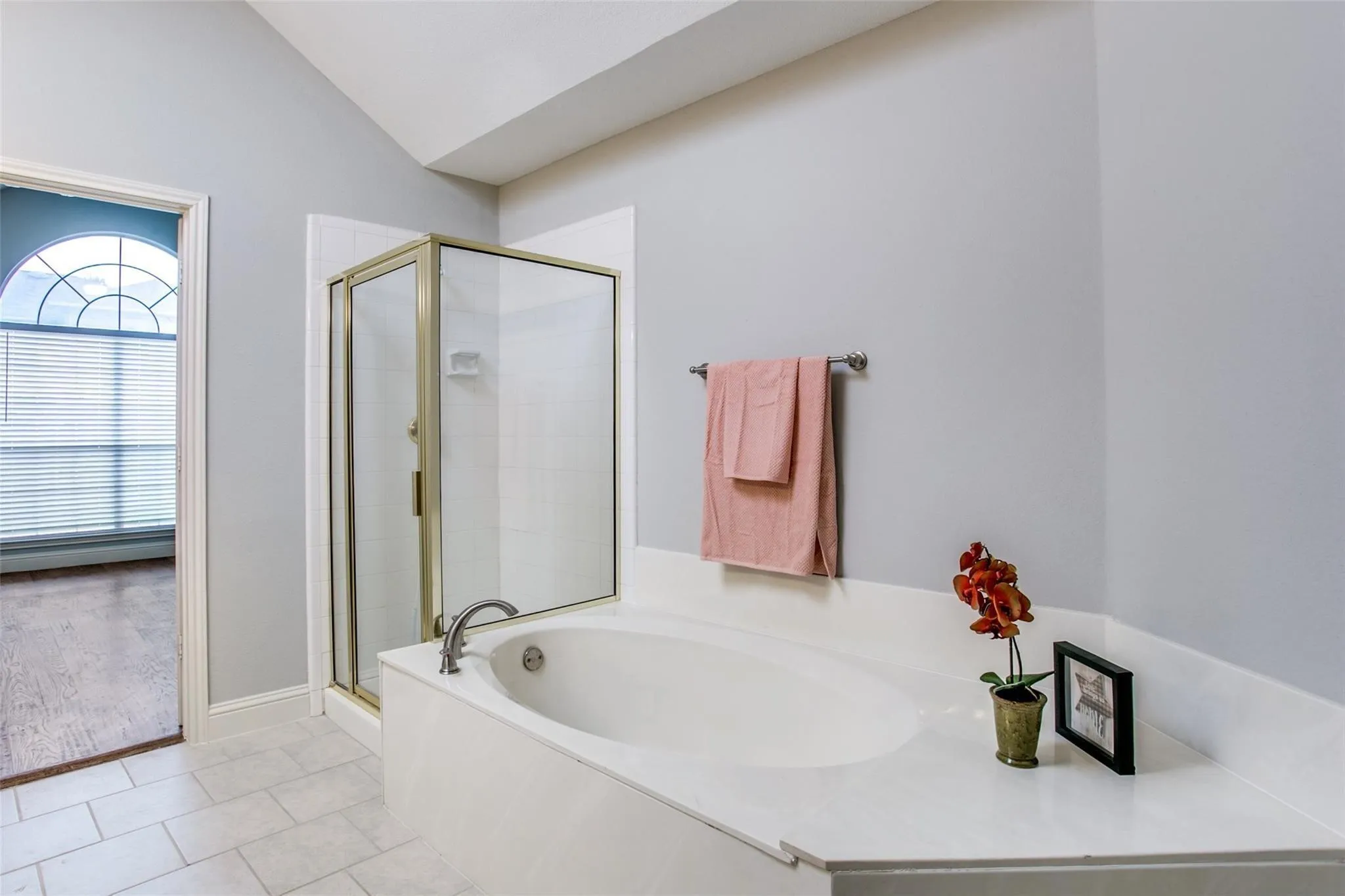 Built-in soaking tub, glass-enclosed shower, light gray wall paint, and light-toned tile flooring