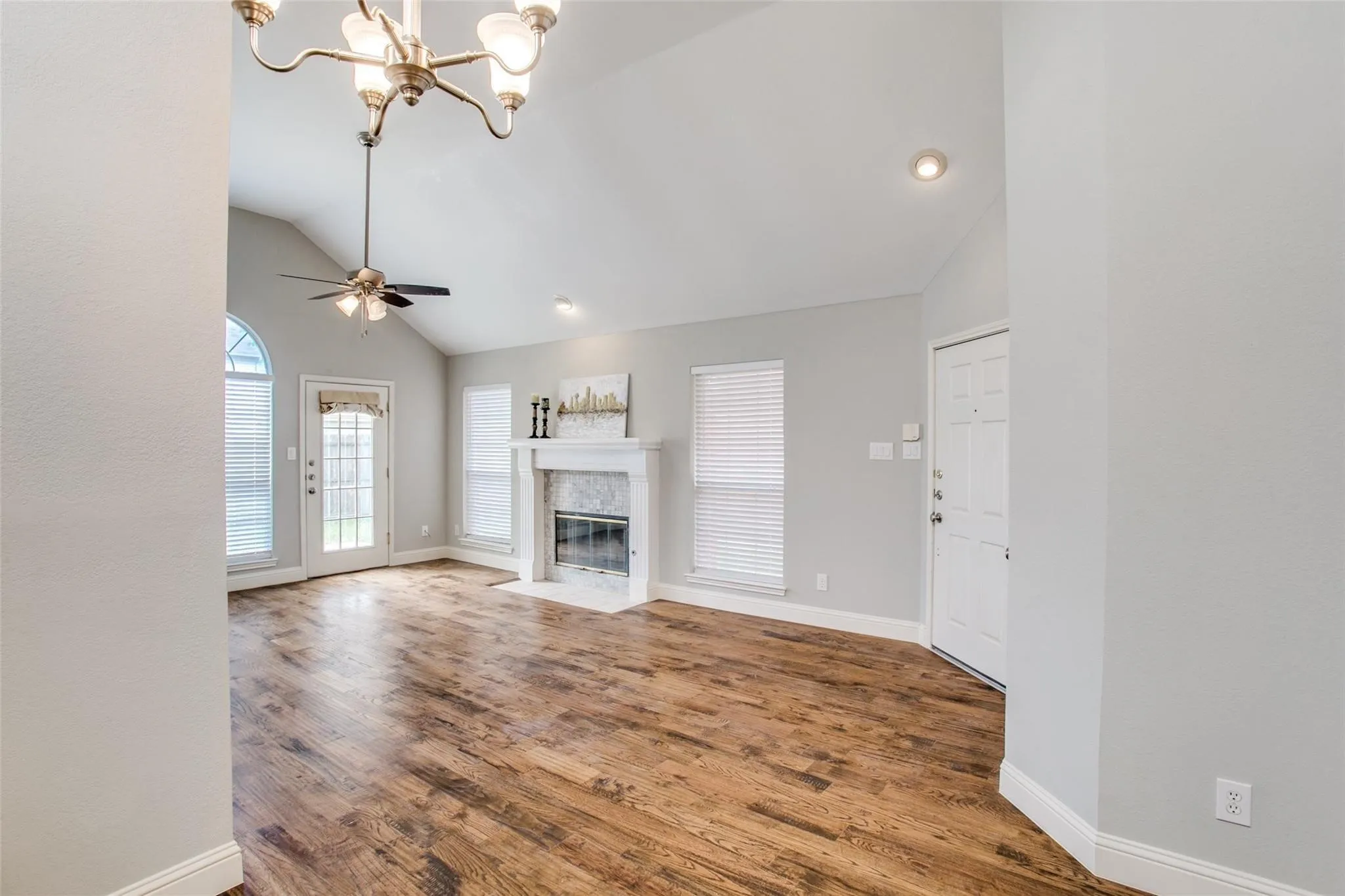 Vaulted ceiling with a ceiling fan, a fireplace with a stone surround, wood-finish flooring, and multiple windows for natural light