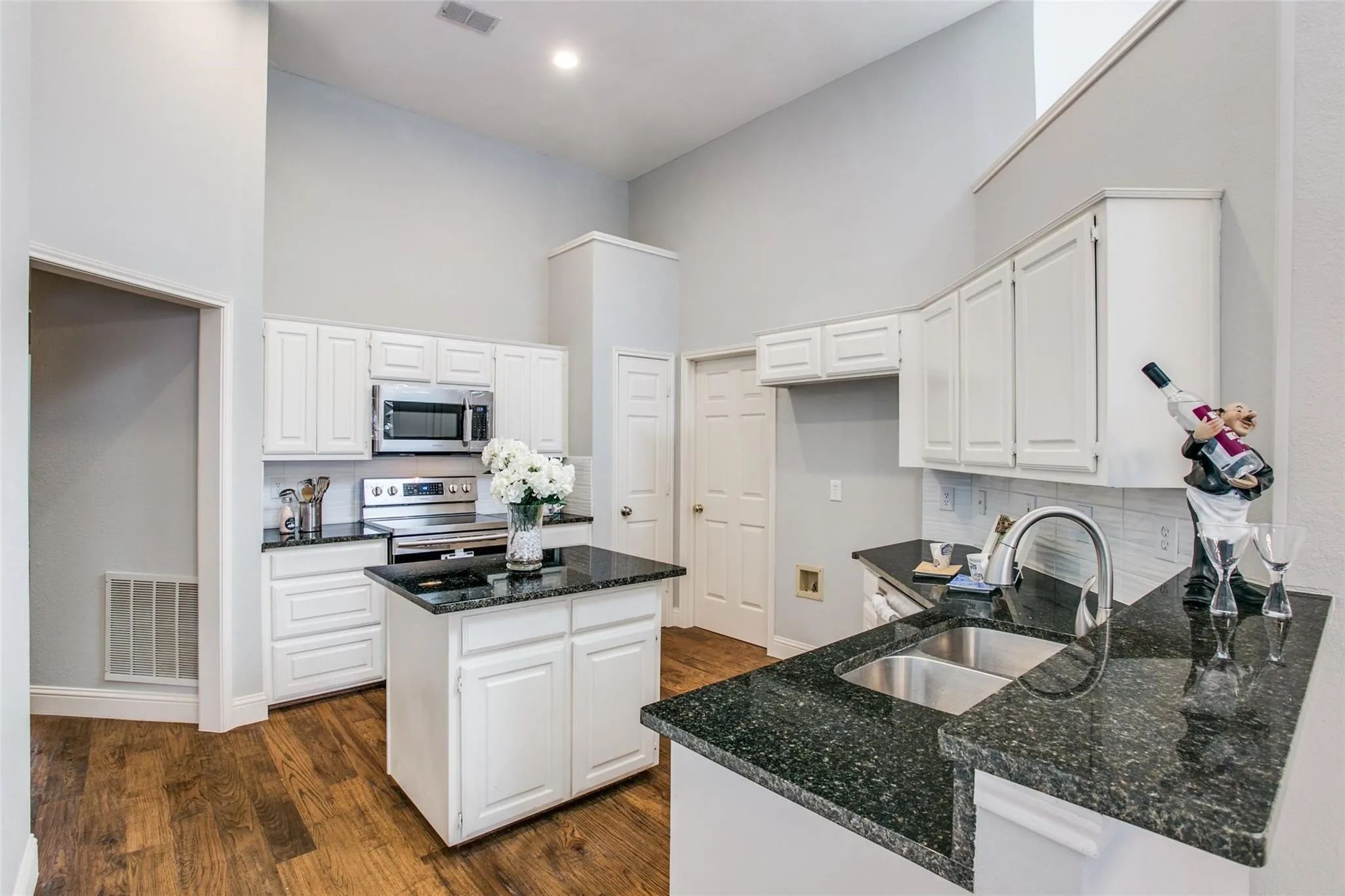 Kitchen featuring white cabinetry, dark speckled countertops, stainless steel appliances, and wood-finish flooring