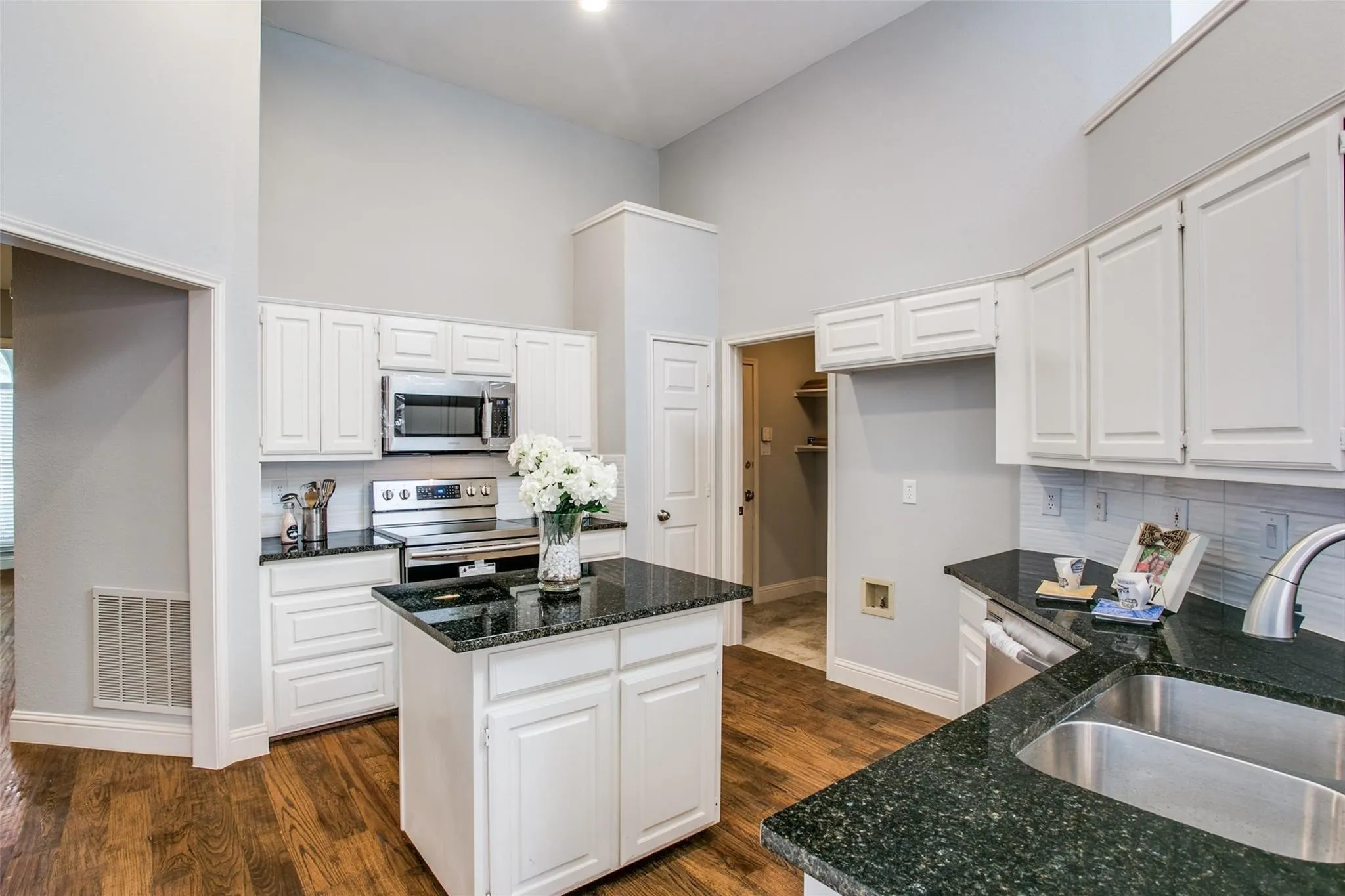 Kitchen featuring dark countertops, white cabinetry, stainless steel appliances, a center island, and wood-finish flooring