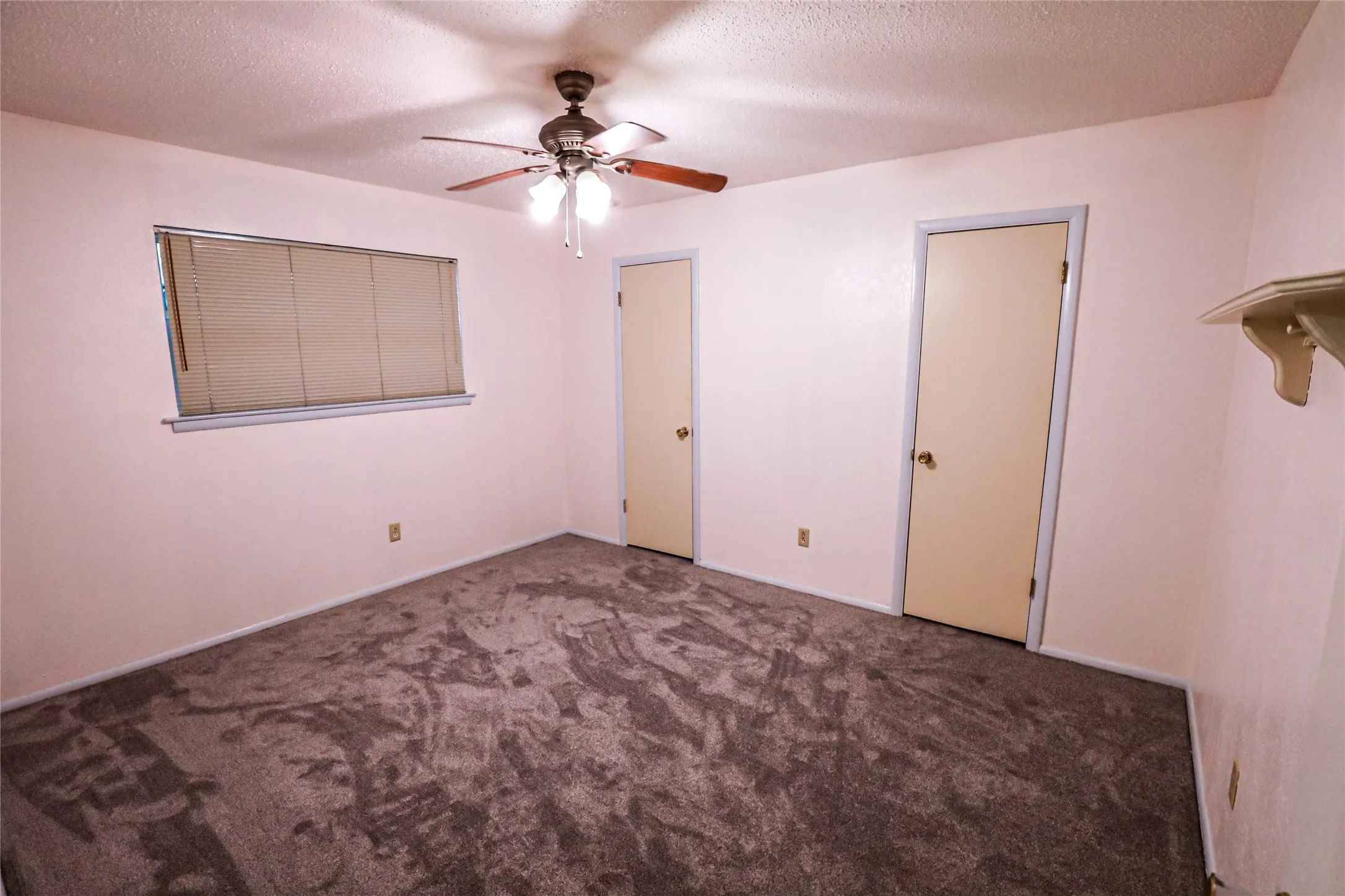Textured carpeting, window with blinds, ceiling fan with integrated lighting, and two interior doors with contrasting trim