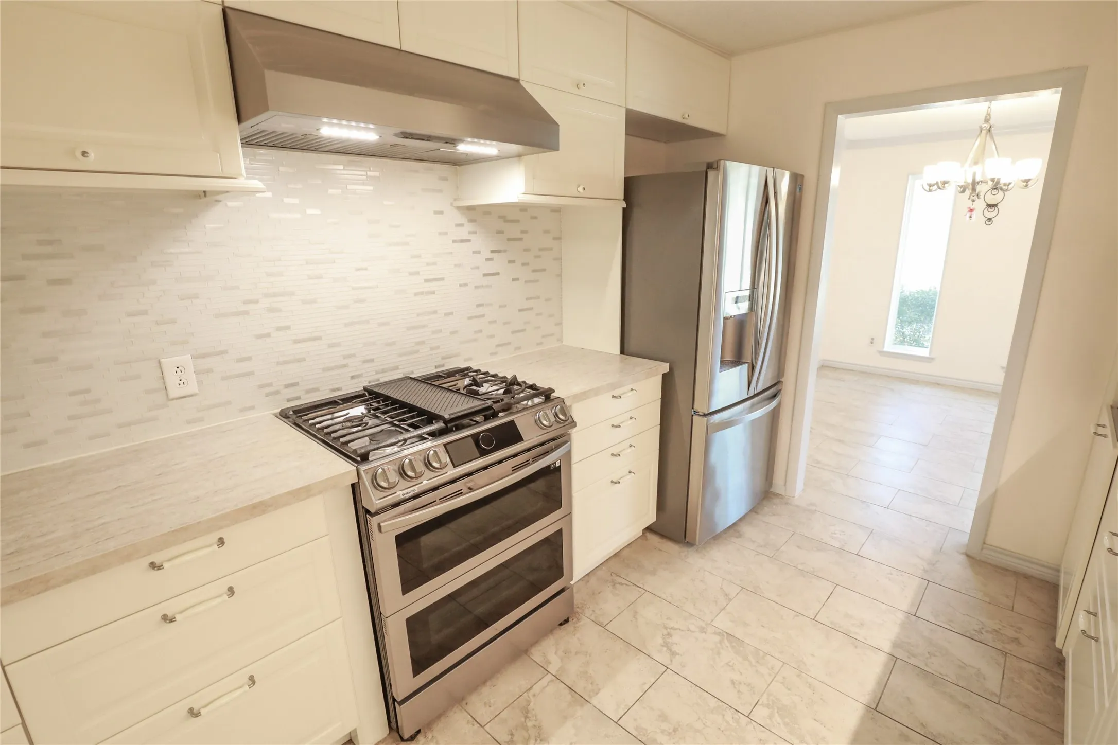 Stainless steel gas range with double ovens, coordinating refrigerator, and white cabinetry