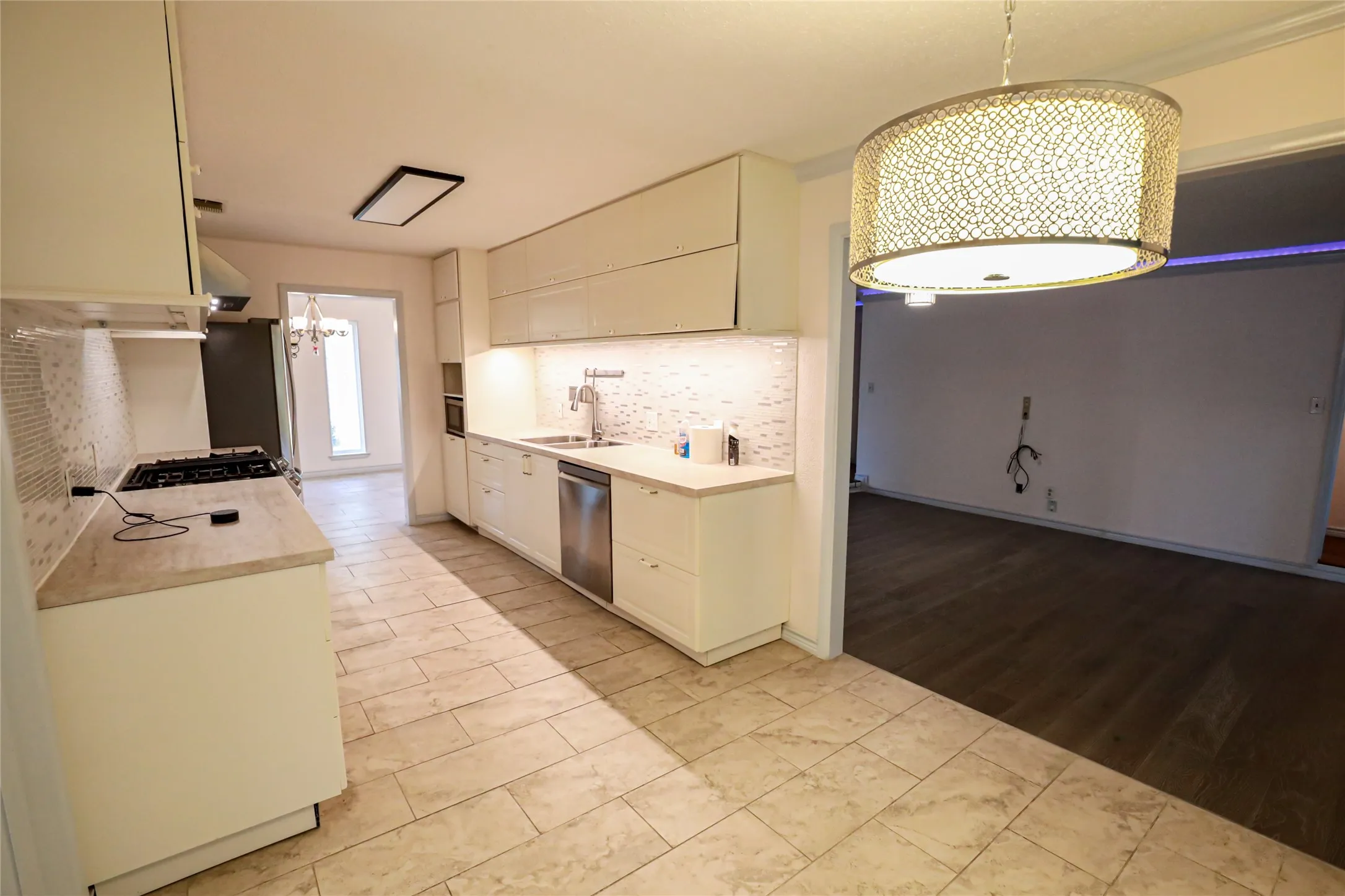 Kitchen featuring light-toned tile flooring, white cabinetry, integrated stainless steel dishwasher, and a gas range