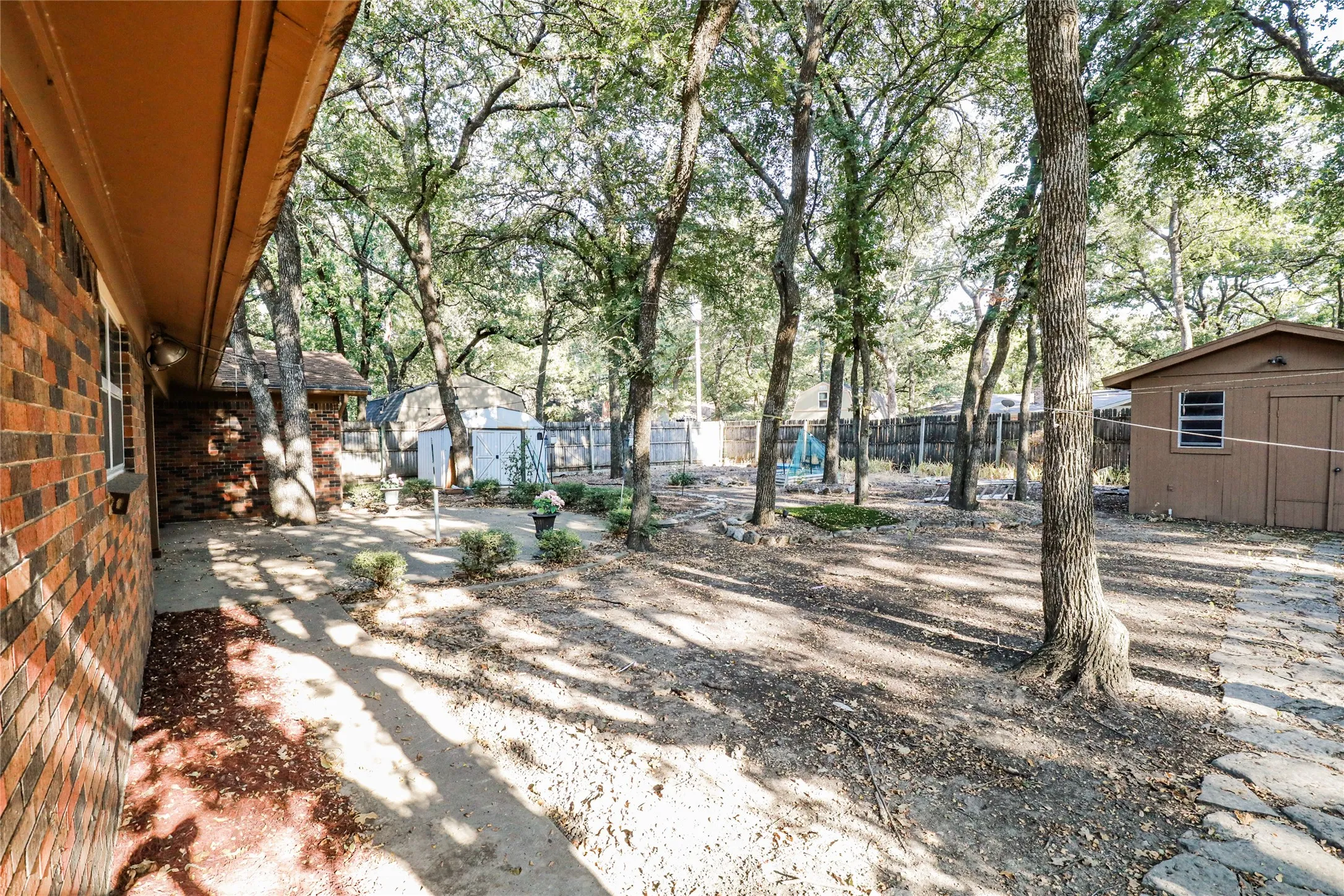 Expansive backyard with mature trees, a detached storage shed, a secondary utility structure, and a brick-clad exterior